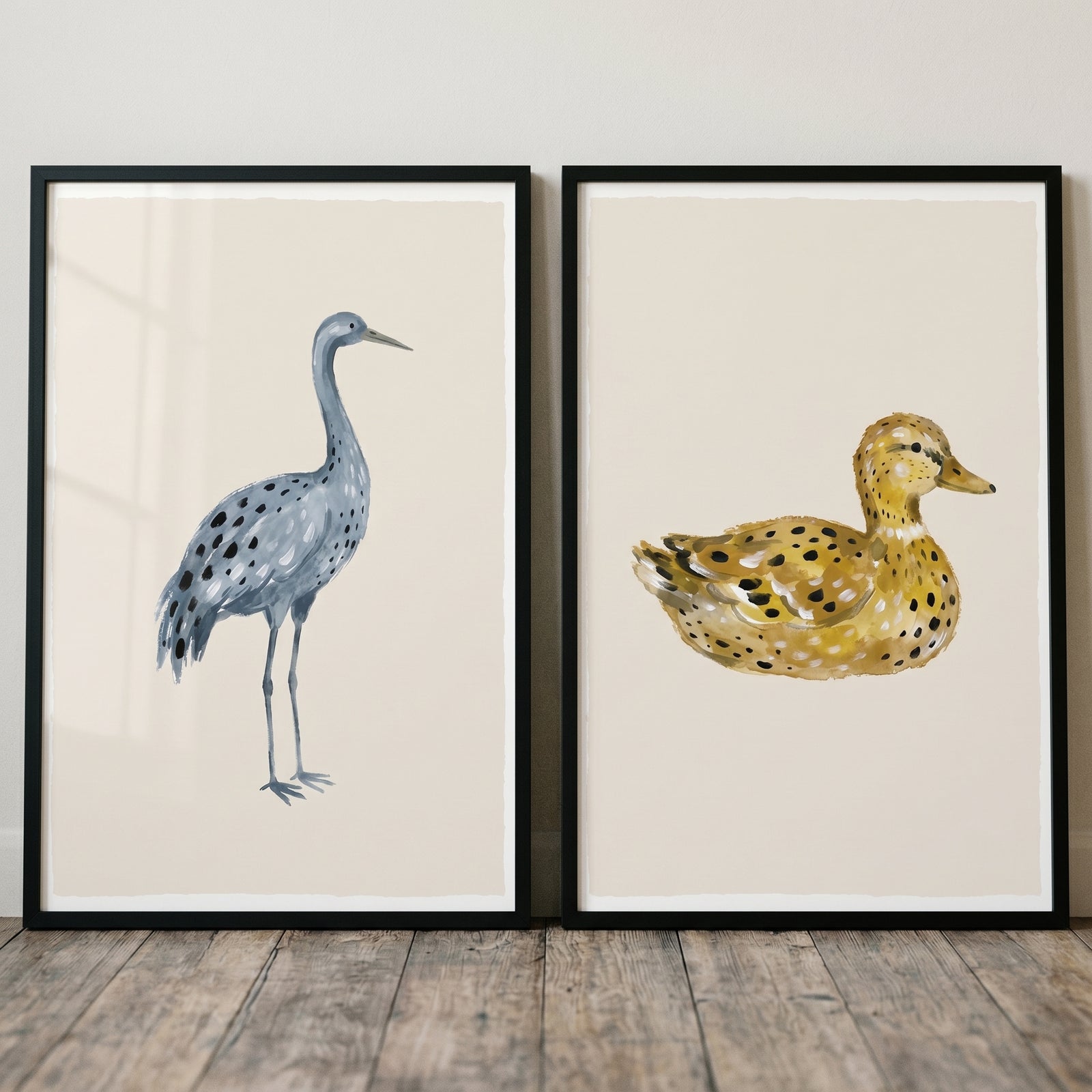 Earthy neutral stippled birds wall art set of 2 featuring a blue crane and a yellow duck in black frames on a wood floor.