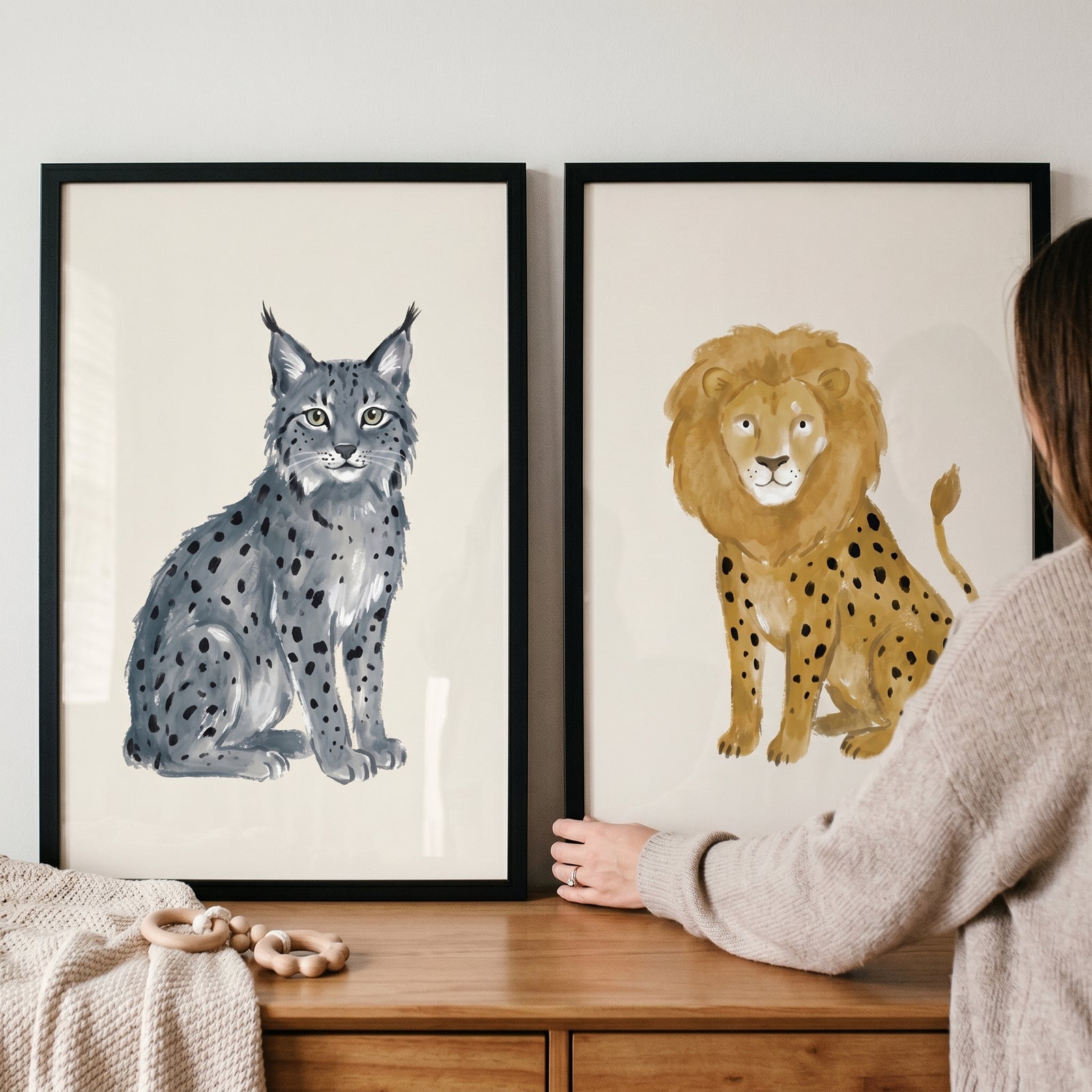Person holding an earthy neutral wild cat artwork set of 2 with a spotted lynx and lion above a wooden dresser.