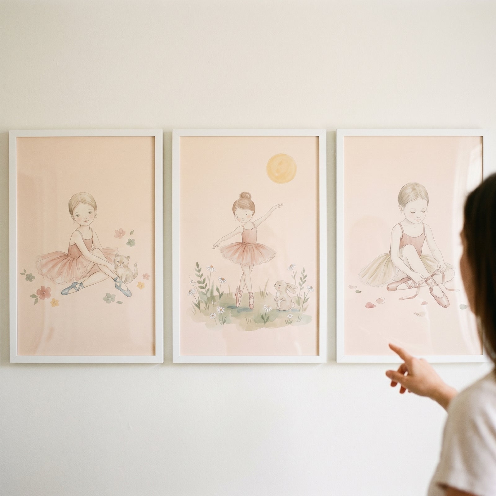 Person points to an earthy pastel leotard ballerina wall art set of 3 featuring young girls and soft nature scenes.