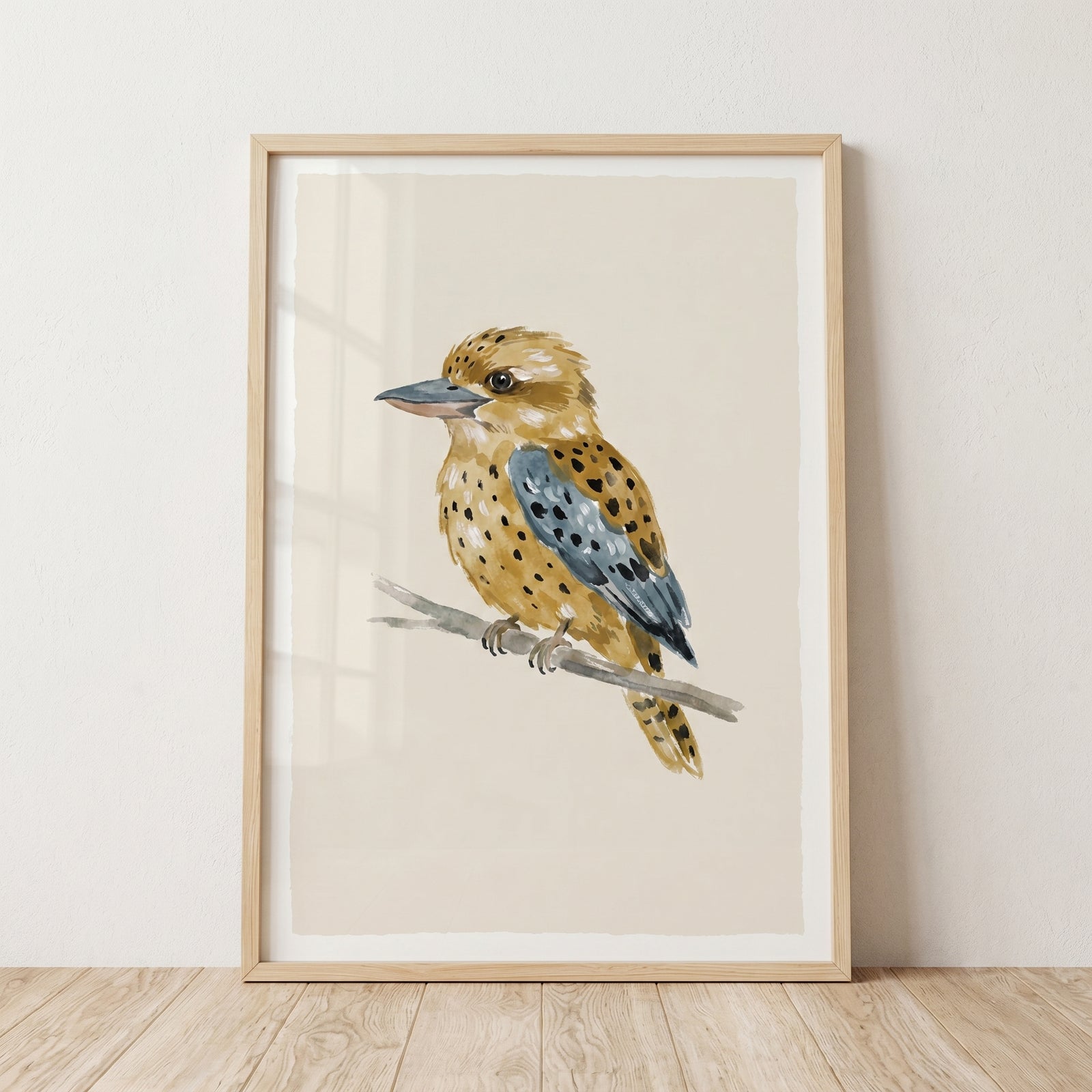 Earthy spotted kookaburra bird wall art in a light wooden frame leaning against a neutral wall.