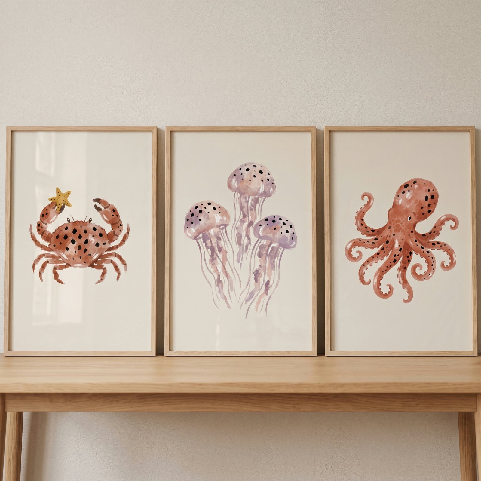 Earthy spotted sea animal wall art set of 3 includes a framed crab, jellyfish, and octopus on a light wood table.