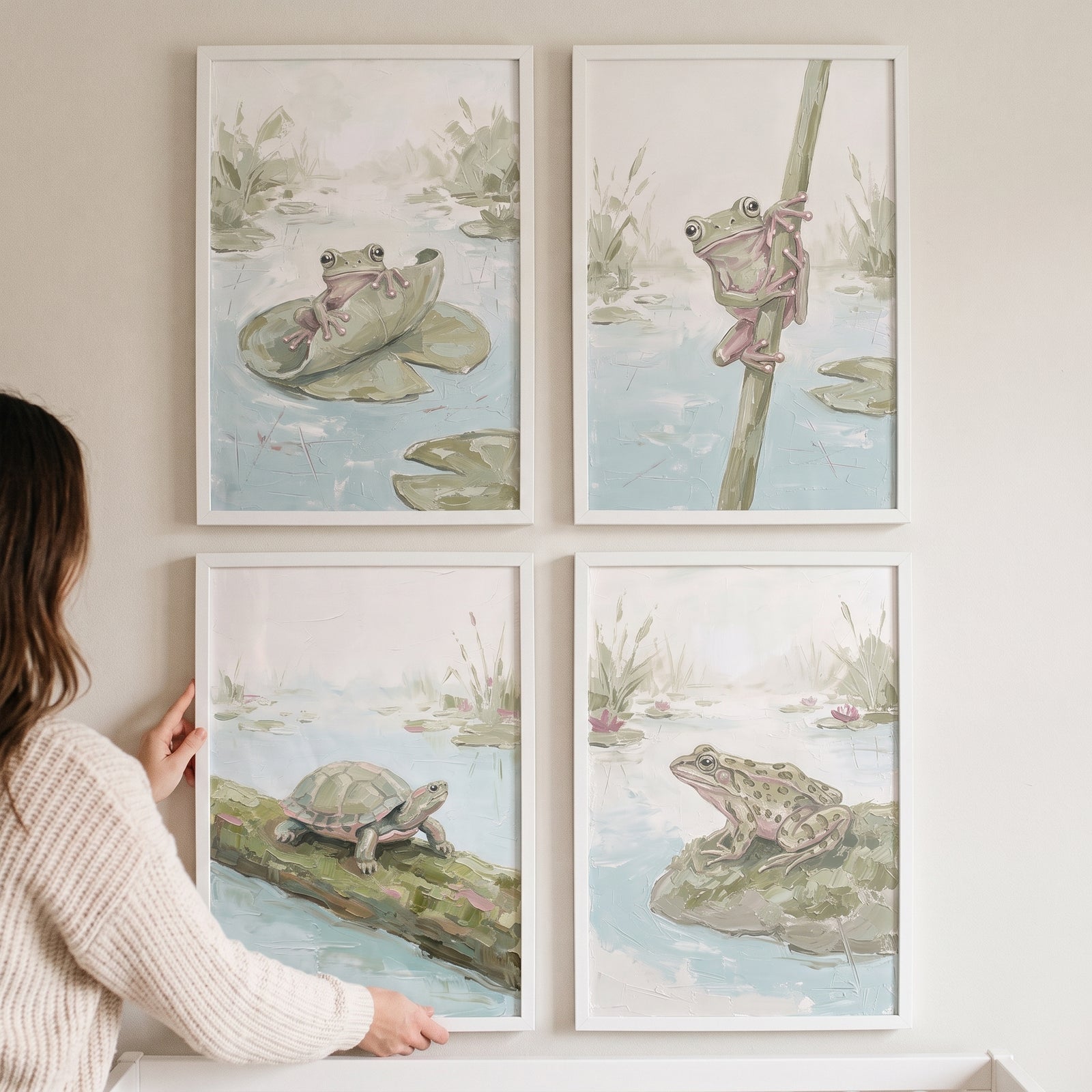 A person hangs an earthy textured pond animals wall art set of 4 featuring frogs and a turtle in soft, muted tones.