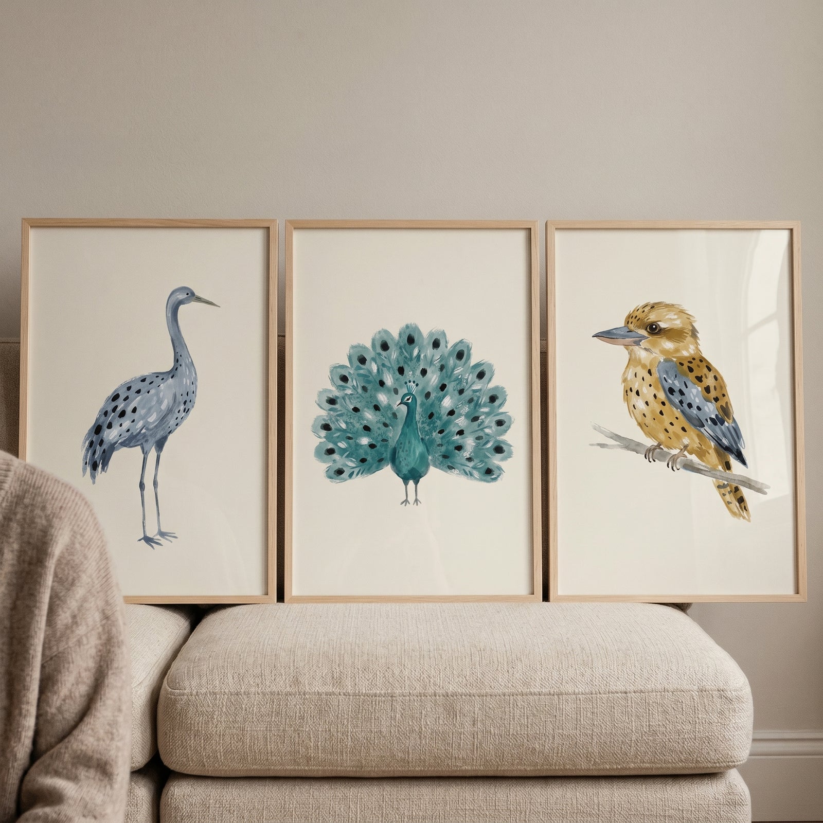 Earthy tonal spotted birds artwork set of 3 includes a crane, peacock, and kookaburra in wood frames on a beige couch.