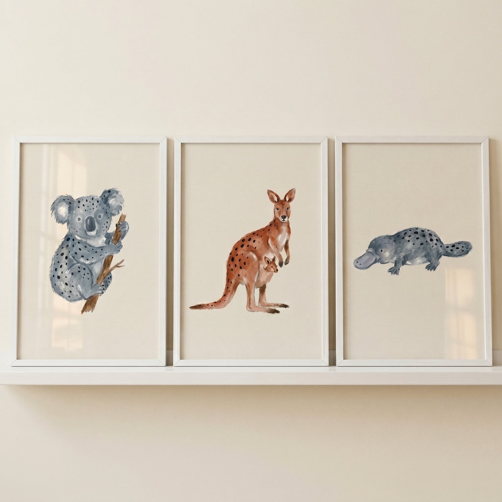 Earthy watercolor australian animals wall art set of 3 featuring a koala, kangaroo with joey, and a platypus on a shelf.