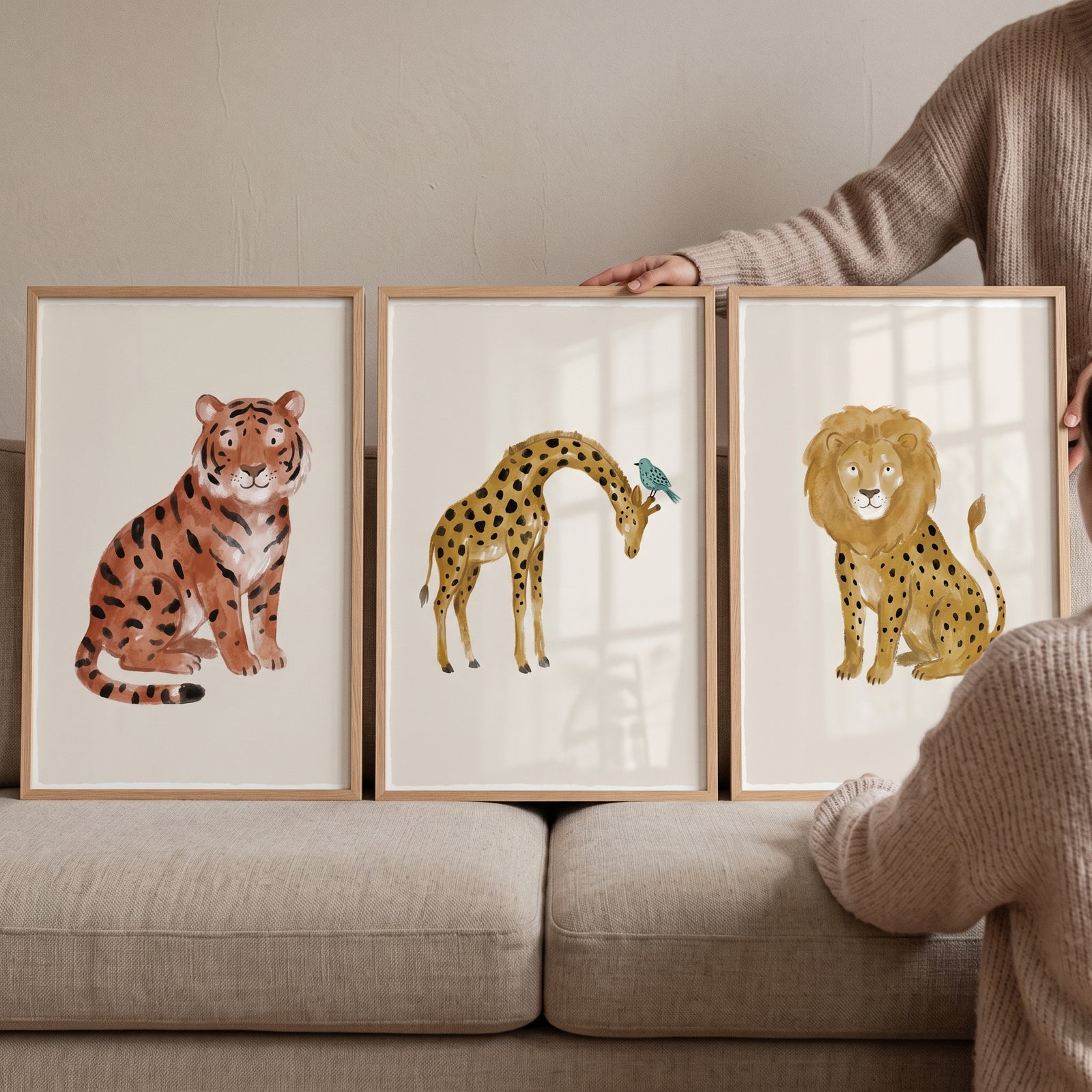 Earthy watercolor safari animal wall art set of 3 featuring a tiger, giraffe, and lion in wood frames on a sofa.
