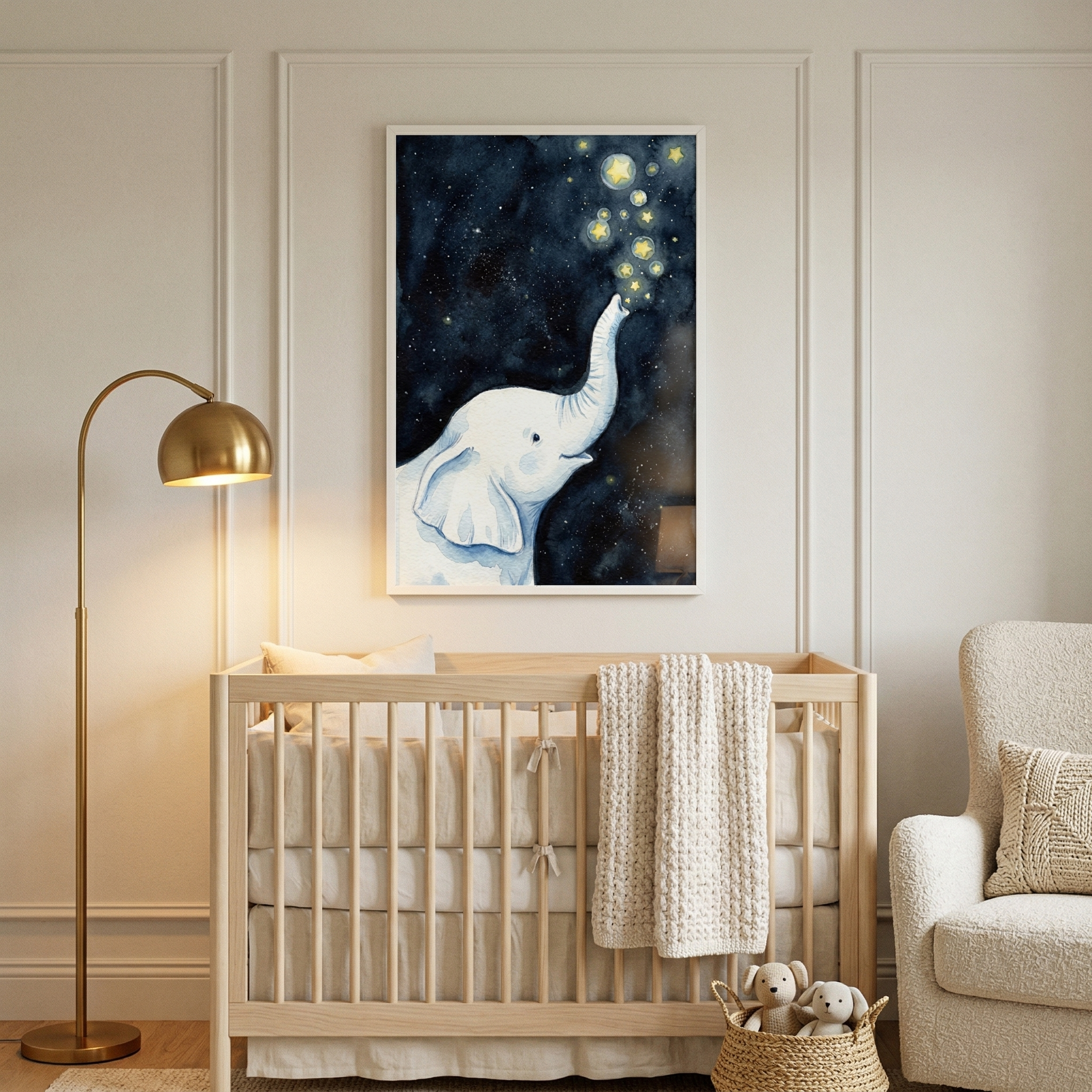 A serene, neutrally-toned nursery features a light wood crib with a cream knit blanket draped over the side. Centered above the crib is a large framed piece of wall art depicting a white watercolor-style elephant blowing glowing stars into a dark blue starry sky. A sleek, gold-finished arched floor lamp stands to the left. To the right, a textured cream armchair sits next to a small wicker basket containing two plush animals. The walls are finished with classic rectangular molding.