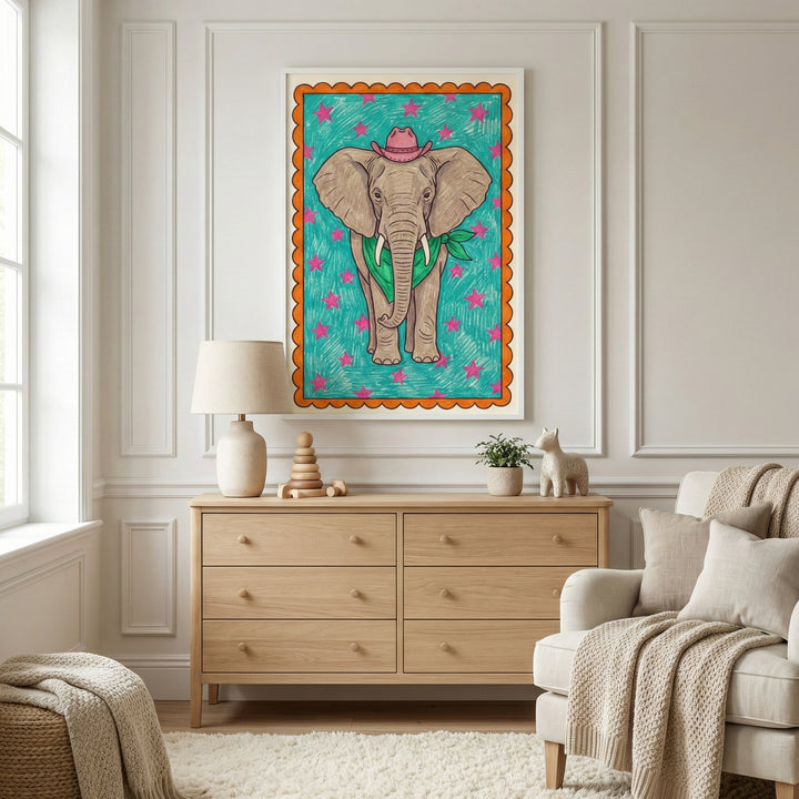 A framed illustration of an elephant wearing a pink cowboy hat and a green bandana hangs above a modern wooden dresser in a bright, neutral-toned room. The space is accented by a cream-colored armchair with textured blankets, a soft rug, and a large window.