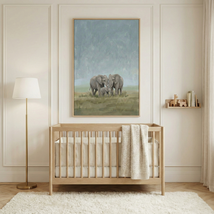 A serene and neutrally-toned nursery features a light wood crib centered in front of a wall with sophisticated molding. Hanging above the crib is a large, vertical framed canvas art piece that illustrates three elephants—two adults and a small calf—walking through a meadow under a soft, hazy blue sky. To the left of the crib stands a tall floor lamp with a gold-finished base and a simple white conical shade. 