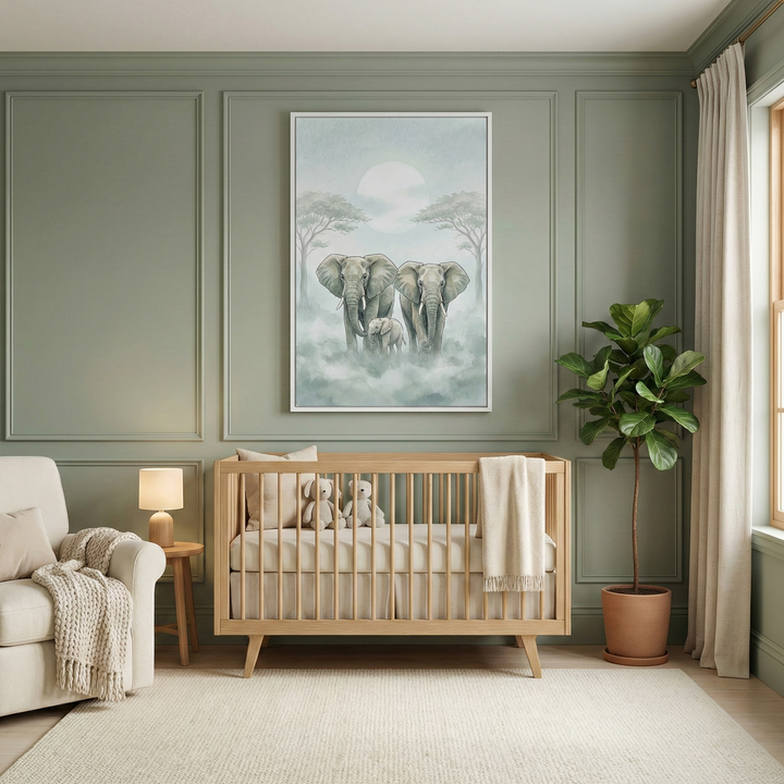 A peaceful nursery featuring a light-toned wooden crib centered against sage green paneled walls. Above the crib, a large framed artwork depicts a family of elephants in a misty outdoor scene with a full moon. Inside the crib are two soft plush toys and a cream-colored knit blanket. To the left, a plush armchair sits beside a small wooden side table with a lit lamp. To the right, a tall green plant in a terracotta pot stands next to floor-length white curtains. 
