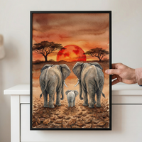 A framed watercolor-style illustration depicts an elephant family, consisting of two large adults and a small calf, walking toward a massive red sun on the horizon. The setting is a savanna with sparse, wide-canopied trees and a ground layered with fallen brown leaves. The sky is rendered in warm washes of orange, red, and brown. A person's hand is holding the black-framed artwork against a white backdrop.