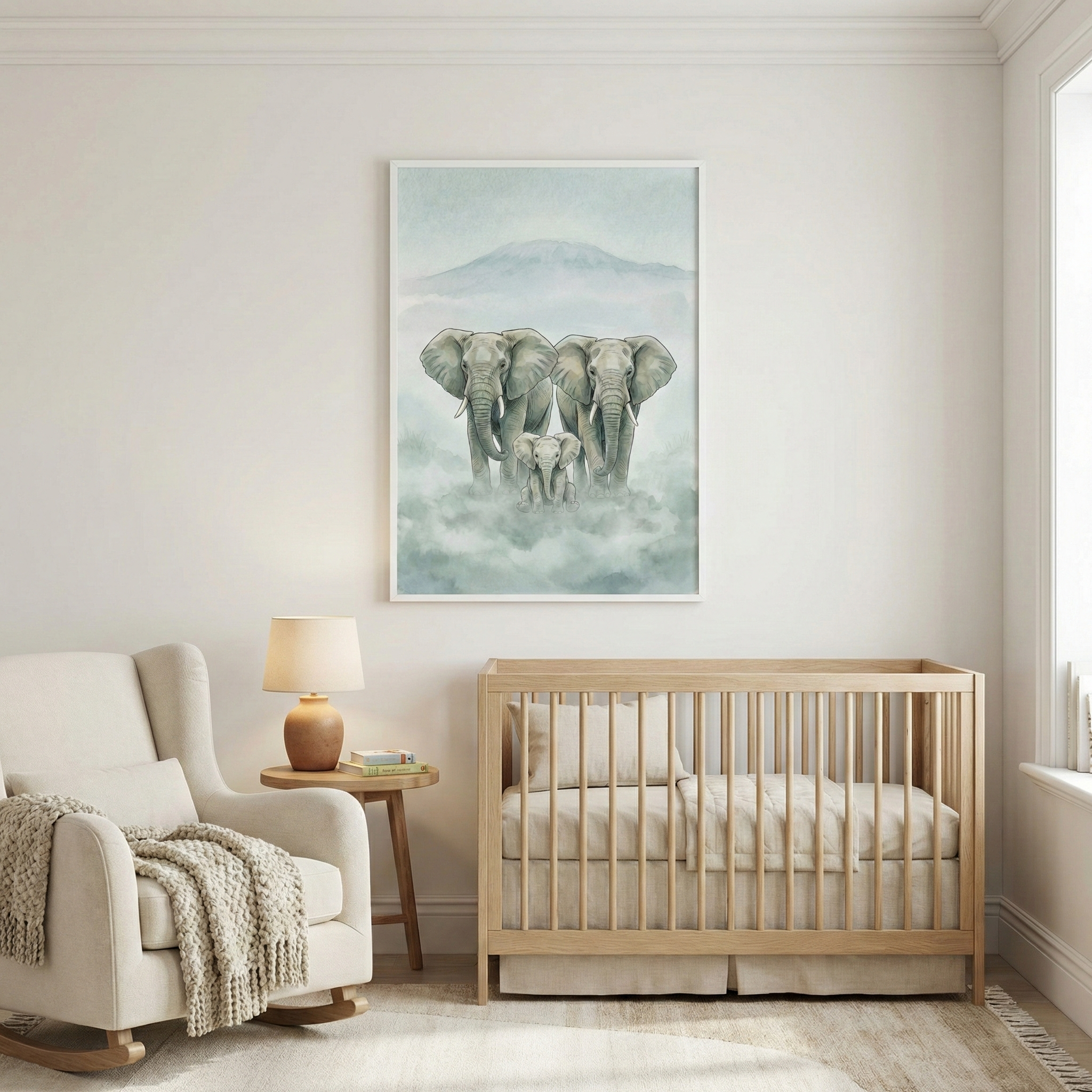 A serene nursery decorated in neutral tones, featuring a light wood crib with beige linens. Centered on the wall above the crib is a large framed vertical artwork showing two large elephants and a smaller calf walking through a misty, mountainous landscape. To the left of the crib is a small wooden side table with a lamp, and a cream-colored rocking chair with a thick knit throw blanket is positioned further to the left on a light-colored rug.