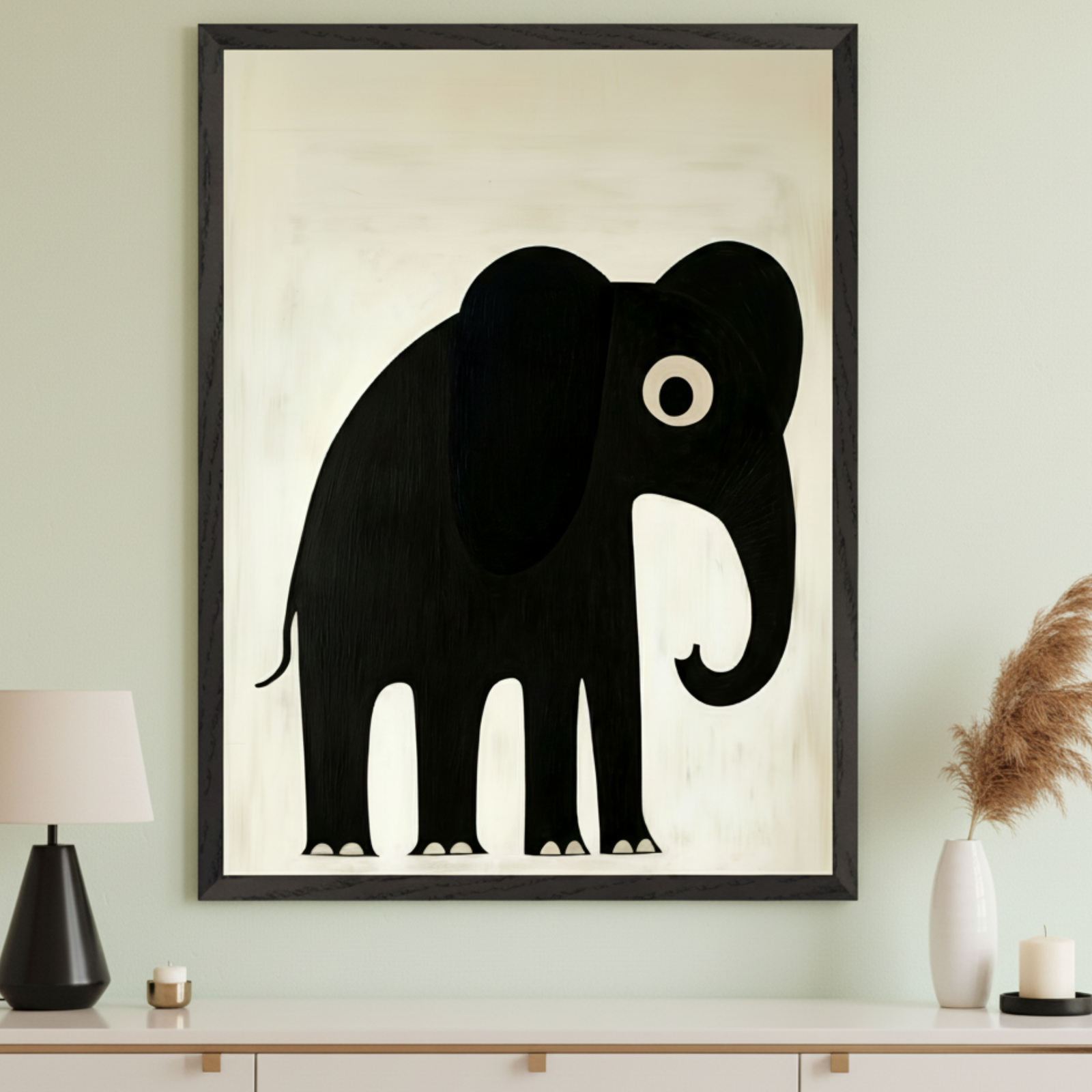 Modern room with a large framed painting of a black stylized elephant on a creamy white background, centered above a white dresser. A black lamp, gold candle, white vase with pampas grass, and a black candle are on the dresser.