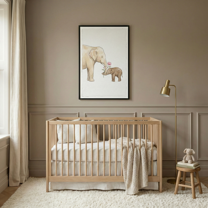 A serene nursery in neutral tones features a light wood crib with white bedding and a chunky knit throw. Above the crib hangs a framed illustration of a large elephant and a baby elephant holding a pink flower. The room includes a slender gold floor lamp and a small wooden stool holding books and a plush rabbit. Large cream curtains frame a window, and a plush rug sits on the floor. The walls are a muted taupe with elegant wall molding, creating a calm atmosphere.