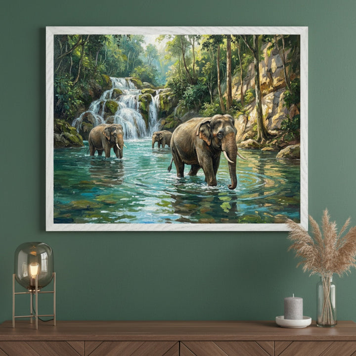 Modern room with a dark green wall and a wooden console table. A large framed painting of elephants in a jungle river with waterfalls hangs above the table. The table holds a lamp, candle, and dried grass in a vase.