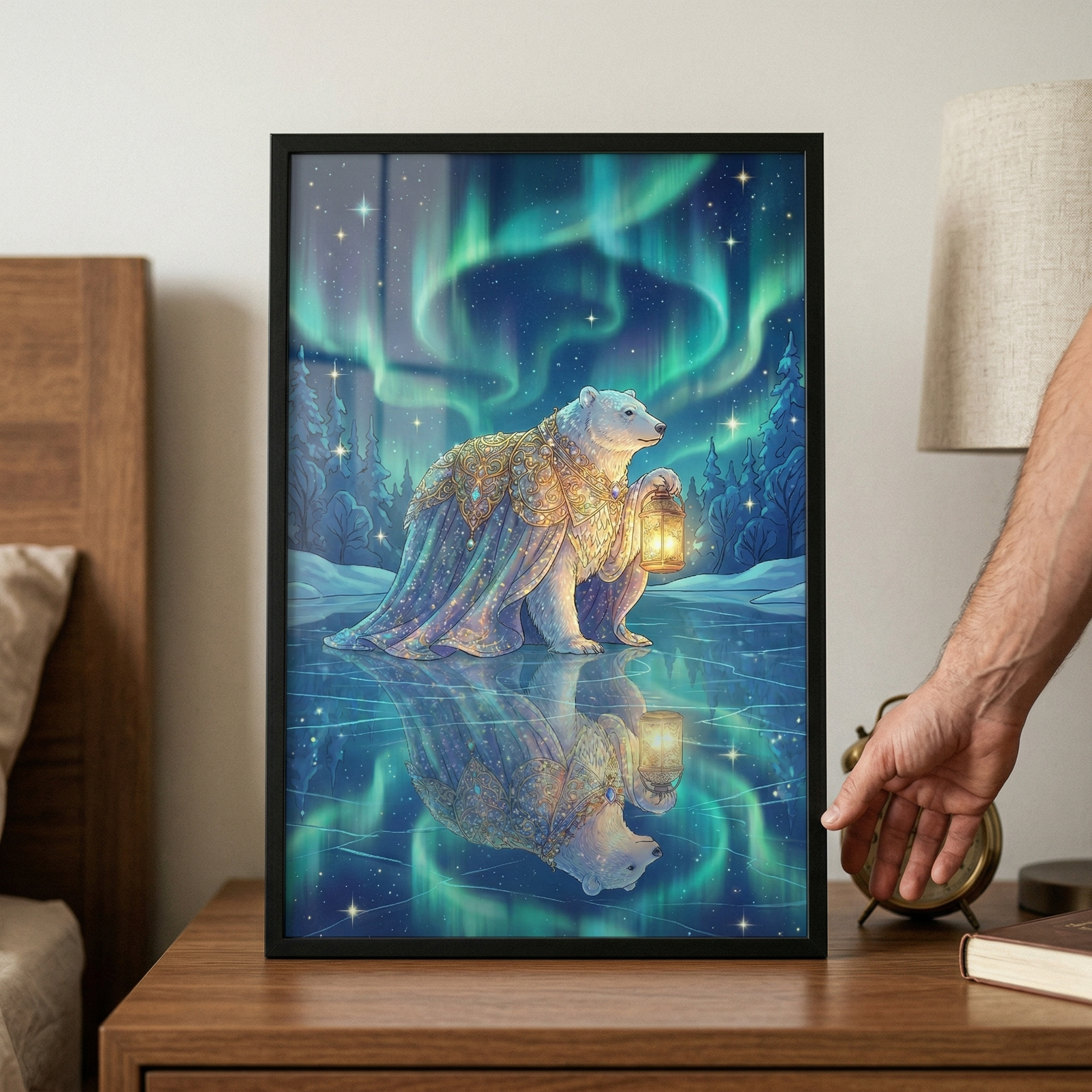 A framed artwork sits on a wooden nightstand, showing an illustration of a polar bear standing on a frozen lake at night. The bear is dressed in an ornate, shimmering blue and gold cape and holds a glowing golden lantern. Above, a vibrant green aurora borealis stretches across a starry sky, and the entire scene is reflected in the glassy ice below. To the right, a person's hand is visible near a small clock, lamp, and book on the table next to a bed.