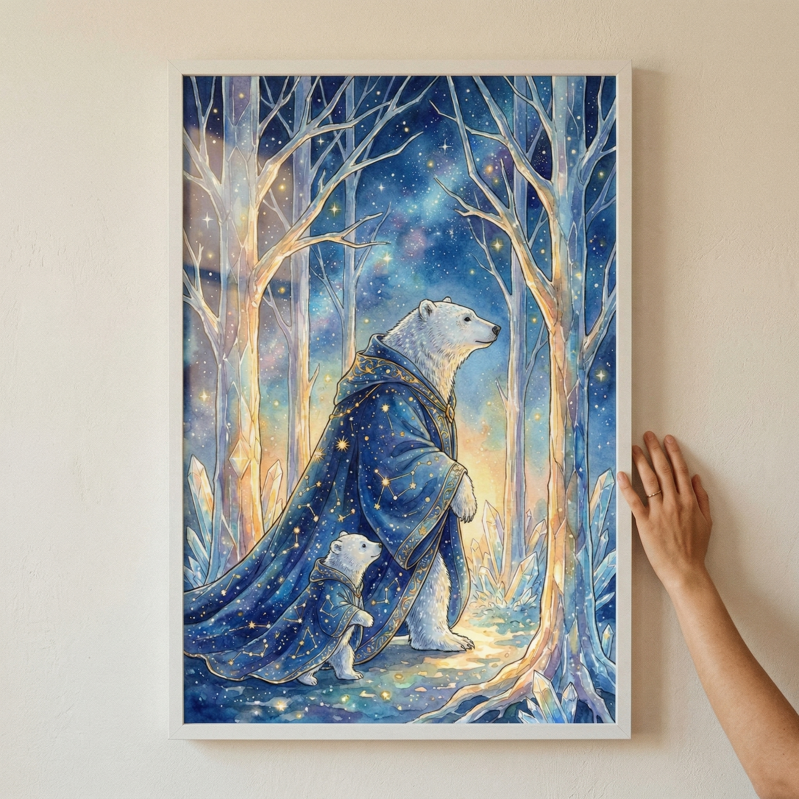 A framed vertical illustration displays a large polar bear and a small cub walking through a mystical, crystalline forest. Both bears are draped in elegant, midnight blue cloaks embellished with intricate gold celestial patterns and constellations. They are surrounded by glowing, translucent trees and jagged ice formations under a vibrant starlit sky. A soft, warm glow emanates from the ground. A person's hand is shown touching the right side of the white frame against a neutral wall.