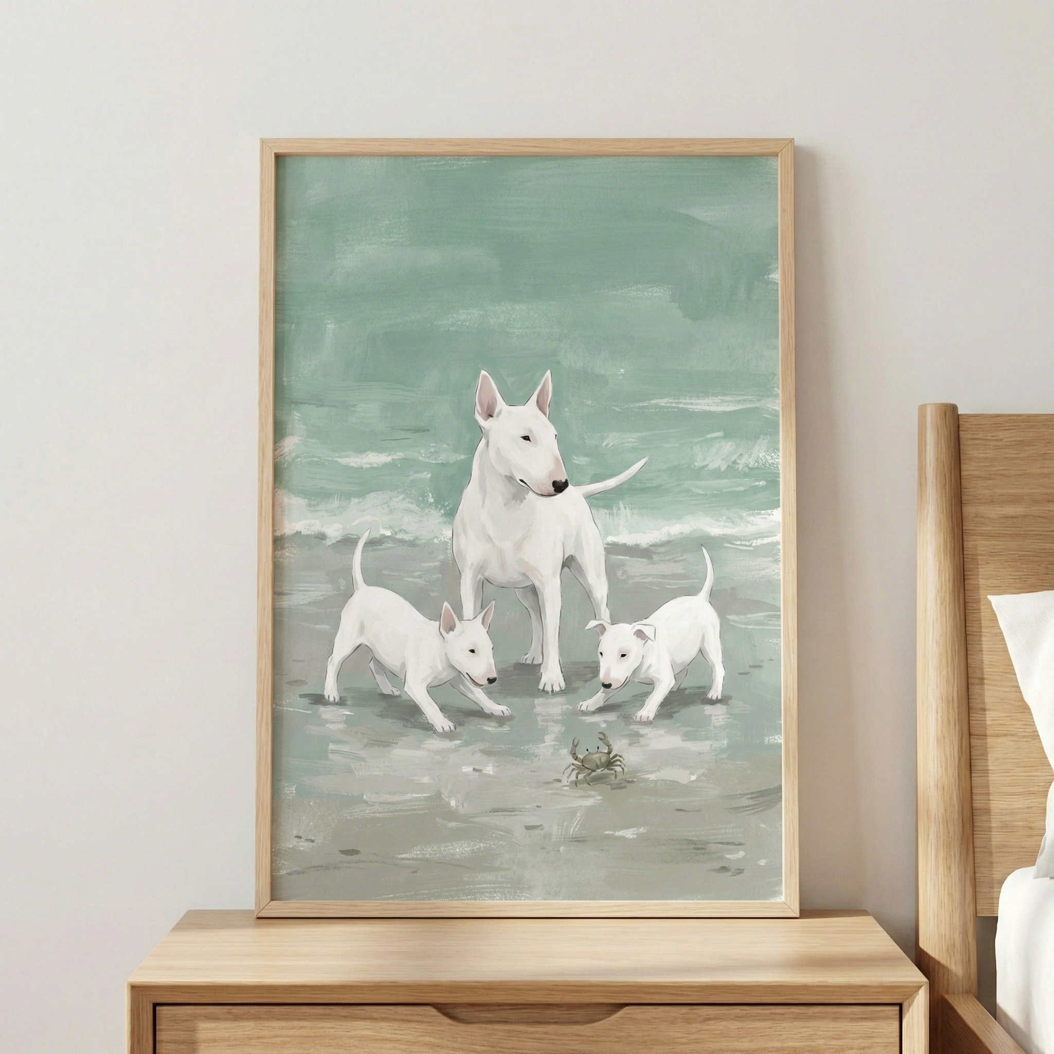 A framed vertical illustration of three white dogs with distinct egg-shaped heads on a beach. An adult dog stands calmly in the middle, while two smaller puppies on either side look down towards a small crab on the sand. The background depicts a calm sea in shades of seafoam green and light grey. The artwork is in a light wood frame, hanging on a neutral-colored wall above a wooden nightstand.