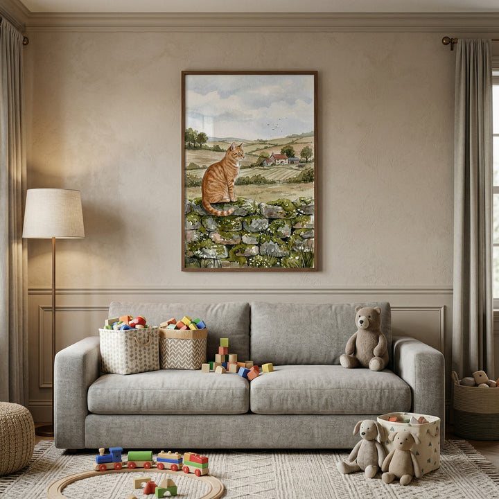 This image depicts a serene and cozy room, likely a playroom or child's nursery, decorated in soft, neutral tones. The focal point is a large, vertical framed artwork hanging on a beige wall. The art shows a ginger tabby cat sitting calmly on a rustic, mossy stone wall. 