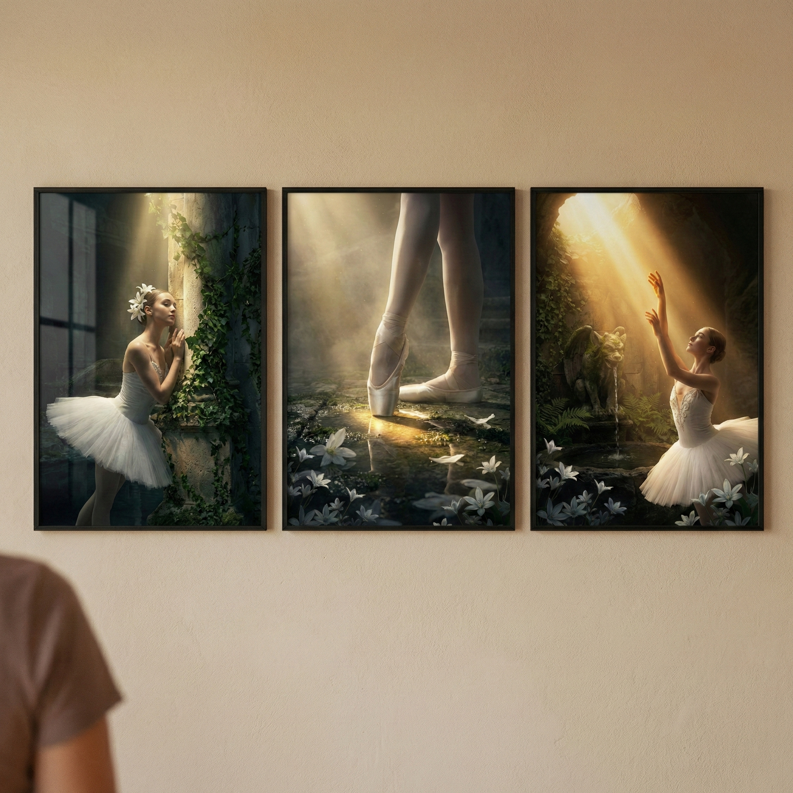 Three framed artworks hang in a row on a plain, neutral wall. The triptych features a classical dancer in various atmospheric settings. On the left, a figure in a white tutu leans against an ivy-draped stone pillar. The center image focuses on a dancer’s legs and feet on pointe, standing on a bed of white flowers under a golden beam. On the right, a dancer reaches towards a bright light in a dark, cave-like space filled with greenery. Each piece is set in a simple black frame.