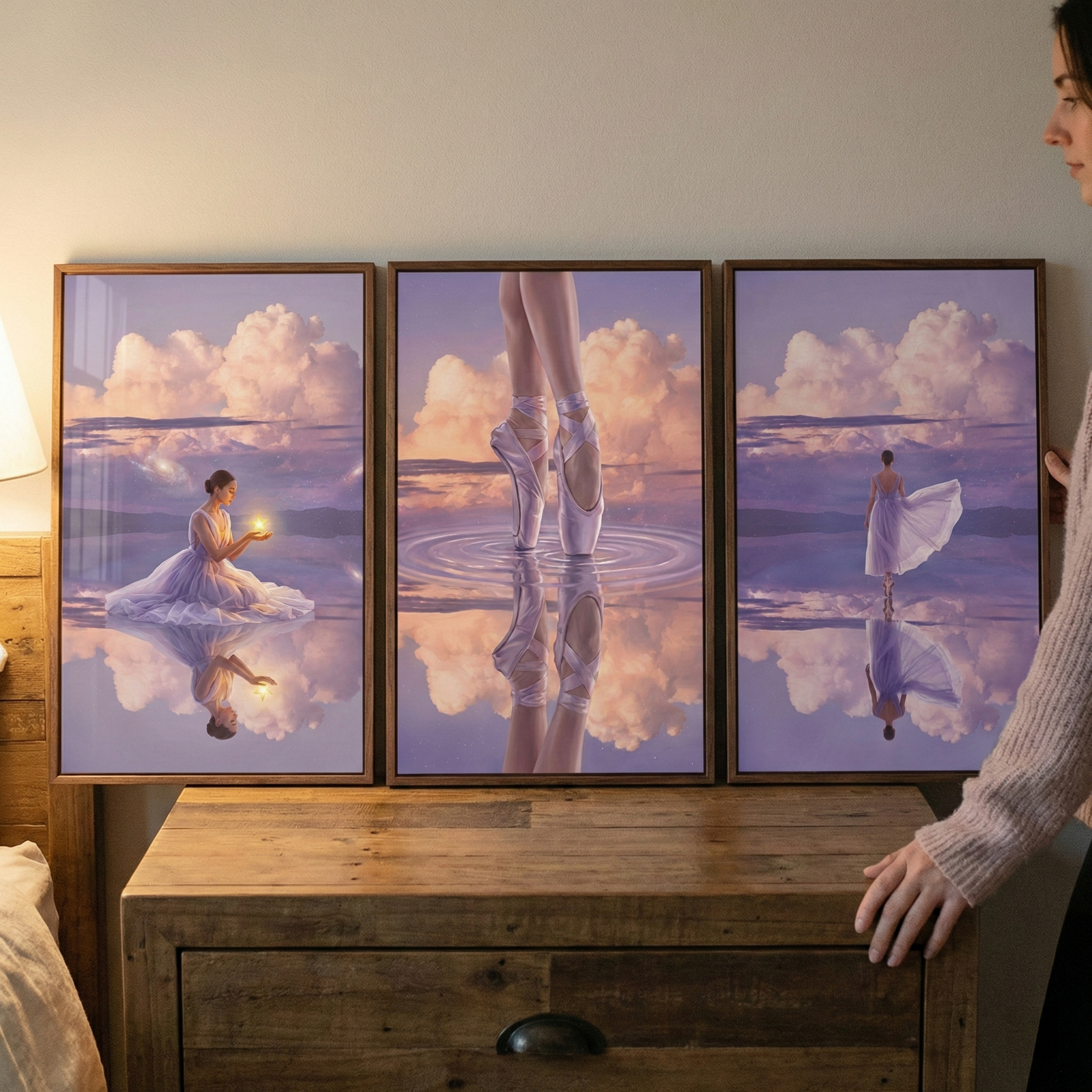 A three-paneled piece of art sits on a rustic wooden dresser against a plain wall. To the right, a woman is partially visible as she stands beside the display. The artwork features a surreal, ethereal scene in shades of purple and pink.

