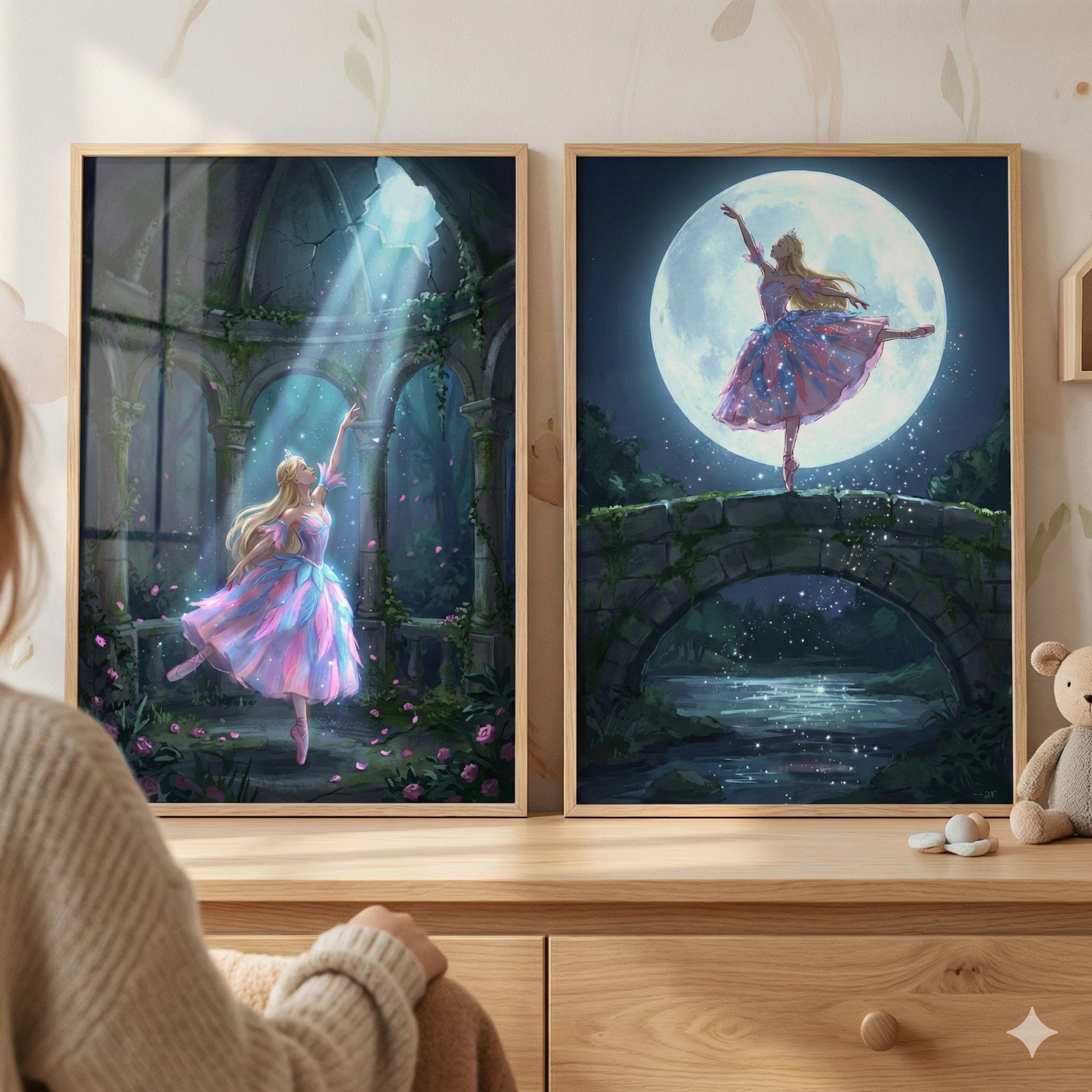 Two framed illustrations of a blonde ballerina rest on a light wood dresser. In the left artwork, she dances in a pink and purple tutu within stone ruins, bathed in a shaft of light from above. In the right artwork, she performs on a stone bridge under the glow of a large full moon, with a river flowing below. A person sits in the foreground, and a small plush bear is visible to the right. The background features light-colored walls with delicate leaf patterns.
