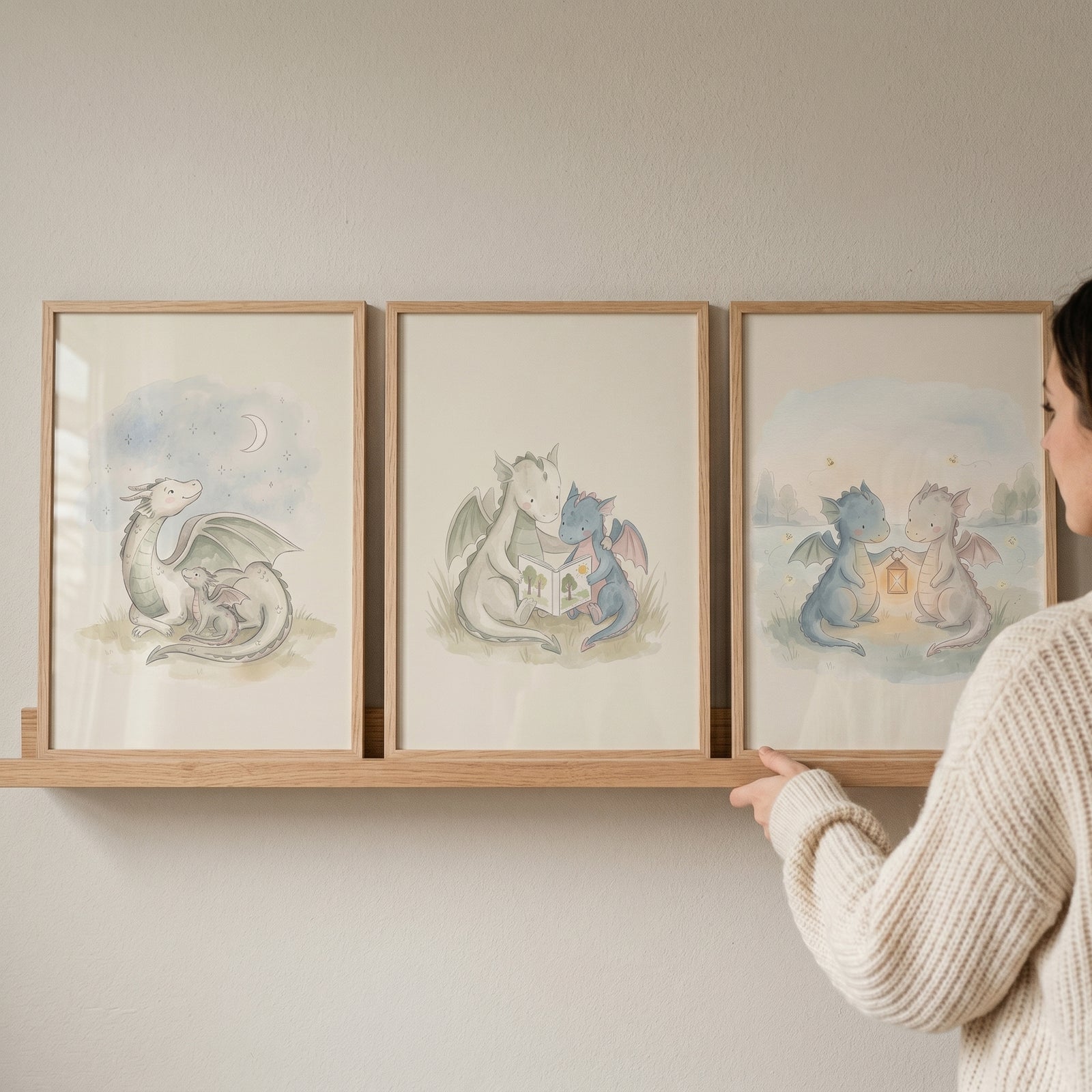 Woman holding an ethereal mythical baby dragons wall art set of 3 in wood frames on a wooden wall shelf.