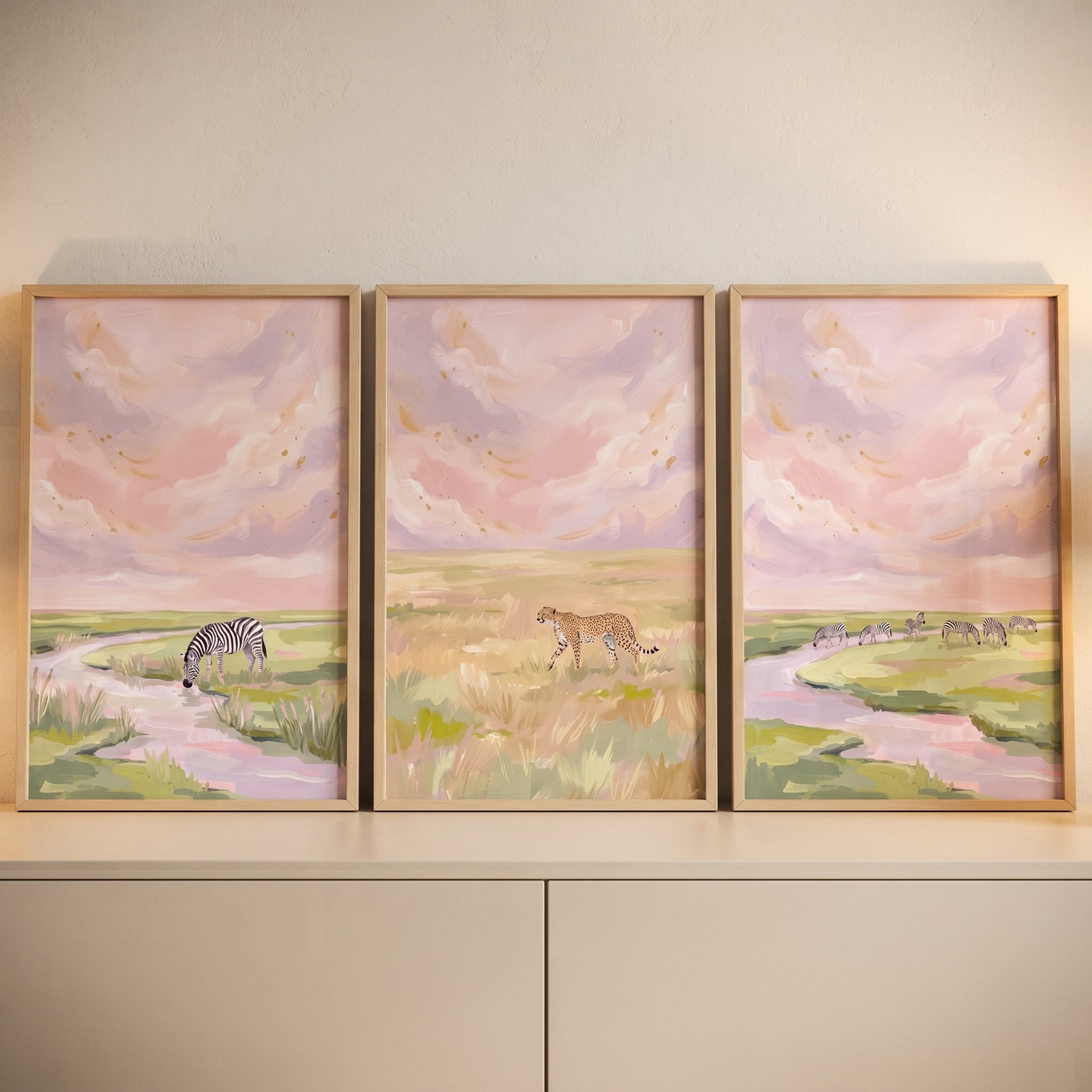 Ethereal pink safari animals wall art set of 3 features zebras and a cheetah in pastel landscapes with soft pink clouds.