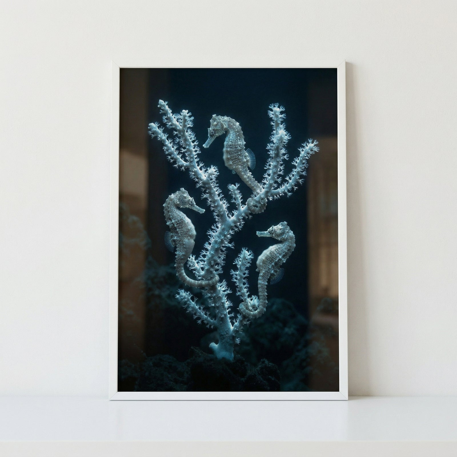 Framed photograph of three seahorses clinging to delicate white coral branches against a deep dark ocean background, creating a serene underwater scene. The artwork’s soft textures and muted tones add a calm and elegant marine inspired focal point.