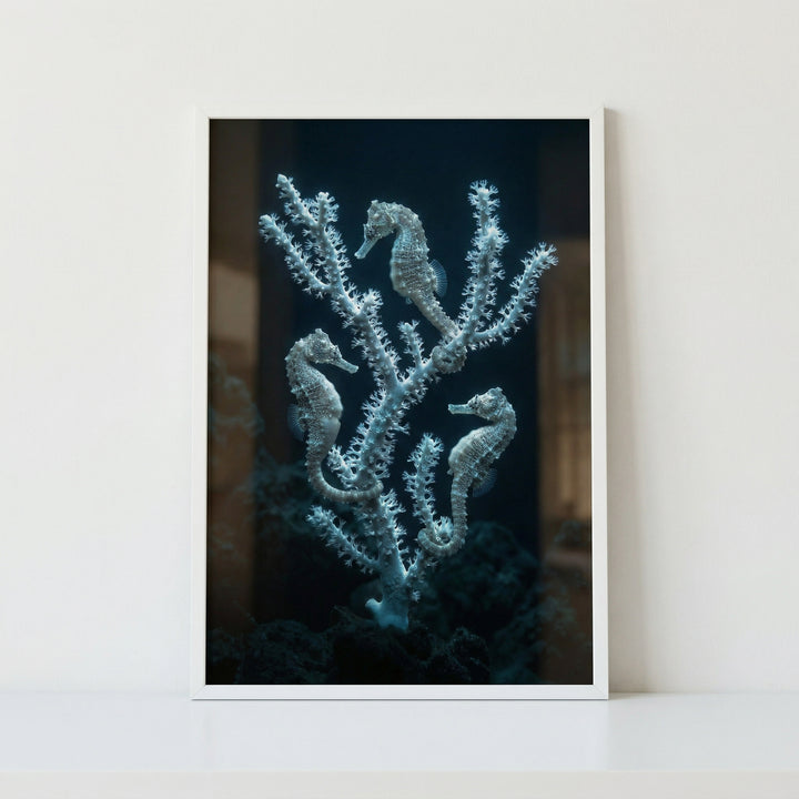 Framed photograph of three seahorses clinging to delicate white coral branches against a deep dark ocean background, creating a serene underwater scene. The artwork’s soft textures and muted tones add a calm and elegant marine inspired focal point.