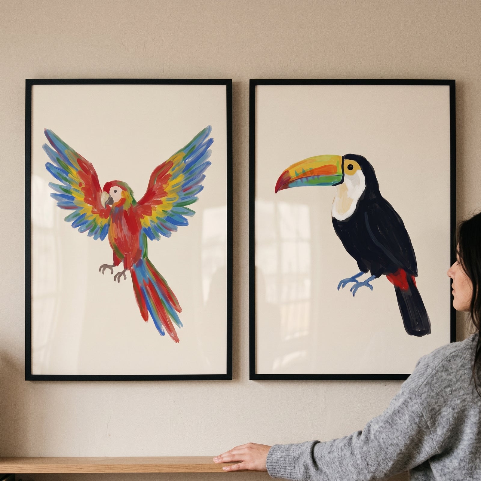 A woman looks at an exotic jungle bird wall art set of 2 featuring a colorful flying macaw and a perched toucan.