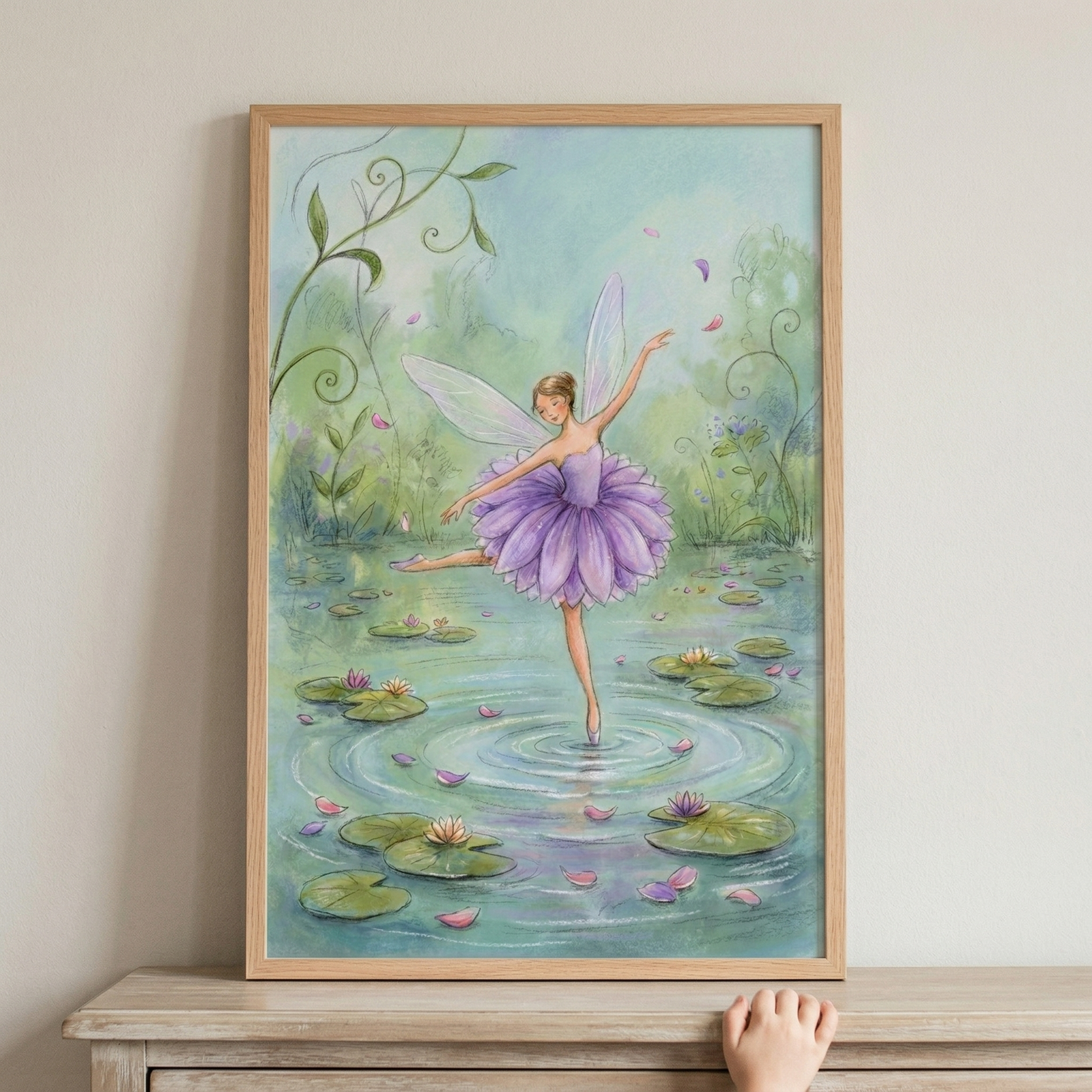 A whimsical illustration of a winged dancer poised in a ballet position on the surface of an enchanted pond. She wears a vibrant purple tutu shaped like flower petals and has delicate, translucent wings. One foot gently touches the water, creating ripples among lily pads and blooming water lilies. The background is filled with soft green foliage and floating pink petals. The artwork is housed in a light wood frame and displayed on a wooden surface.