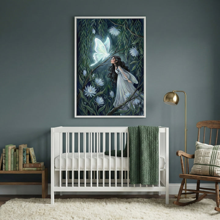 A serene nursery room with a white wooden crib centered against a dark teal wall. Above the crib hangs a large framed piece of art depicting a young woman in a flowing white dress in an enchanted forest, gazing at a large, luminescent white butterfly. To the right of the crib sits a wooden rocking chair with a patterned pillow and a gold floor lamp. To the left, a small wooden bench is topped with several books. A soft, textured white rug covers the floor, and a dark green knit blanket is draped over the ed