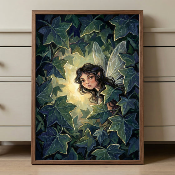 A framed painting of a whimsical woodland fairy with translucent wings and wavy dark hair, peeking out from dense ivy leaves. A soft golden glow surrounds her, creating a magical, mysterious ambiance. The artwork leans against a light-colored dresser in a softly lit room.