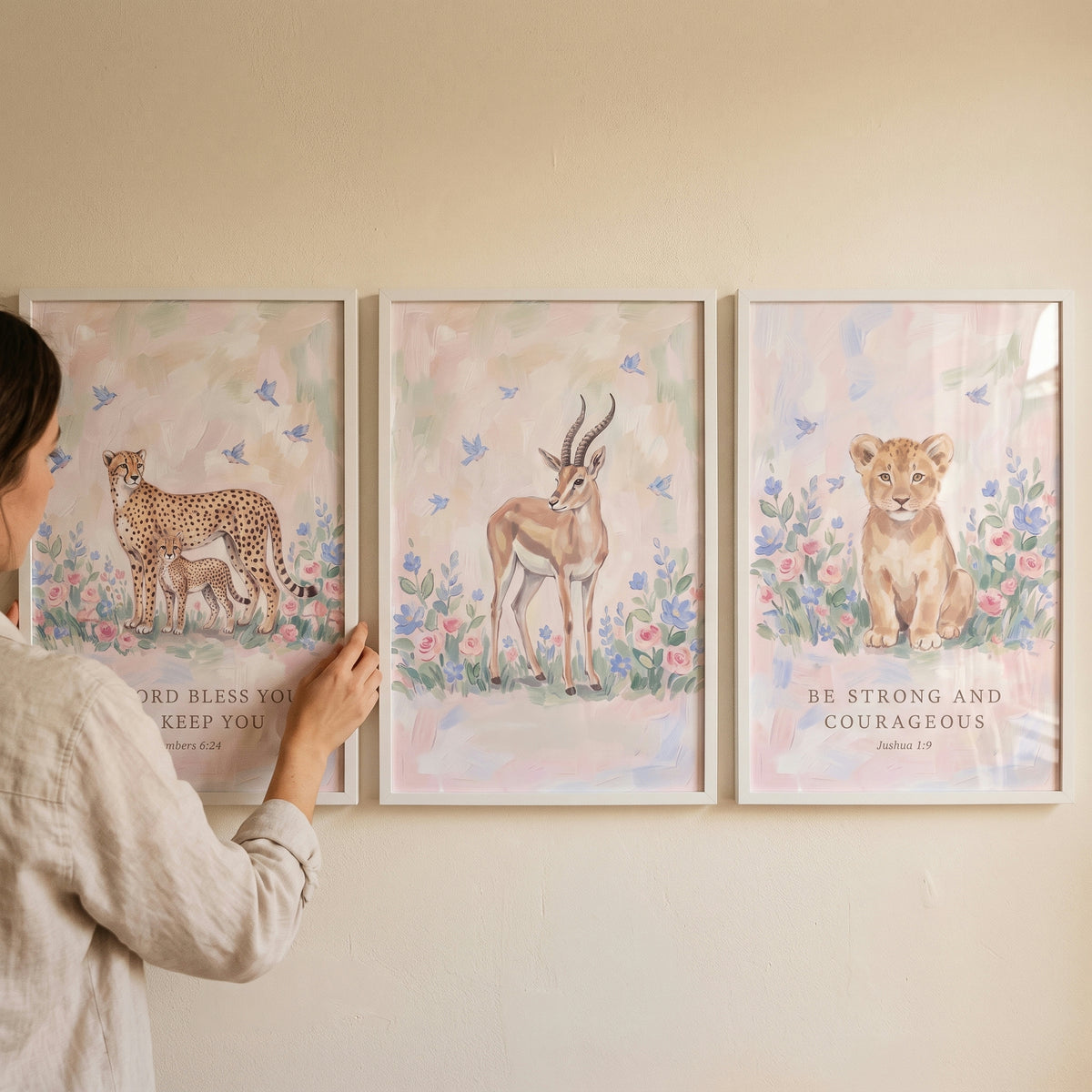 A woman hangs a faith based safari animals wall art set of 3 featuring a cheetah, gazelle, and lion cub with scripture.