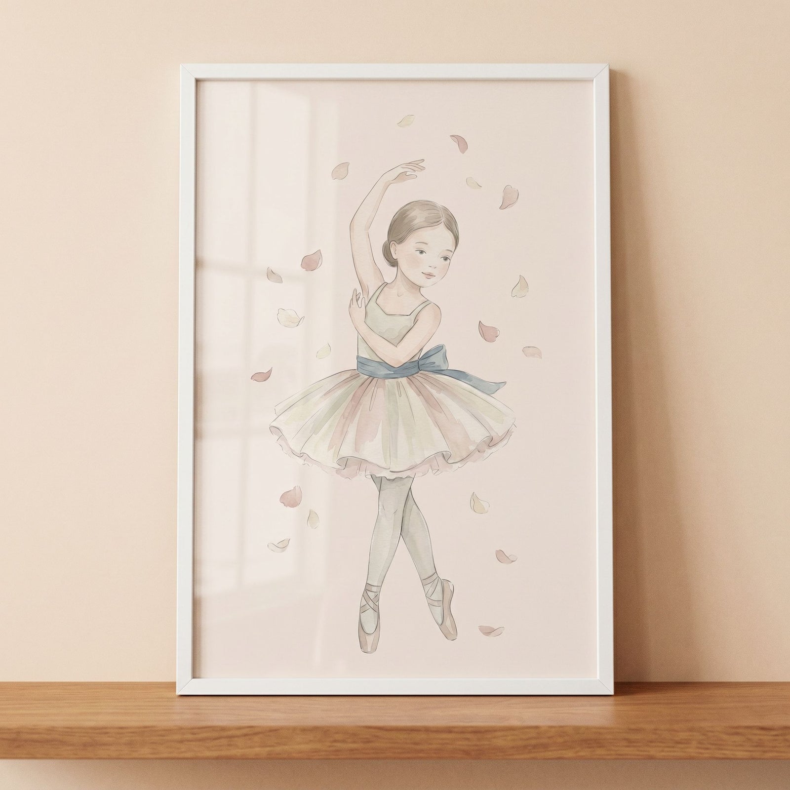 Falling petal watercolor ballerina wall art in a white frame on a wooden shelf shows a girl in a tutu among soft petals.