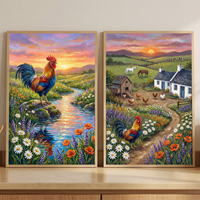 Two colorful framed countryside paintings lean against a wall on a wooden surface. The left painting shows a rooster standing on a rock beside a winding stream surrounded by wildflowers at sunset while the right painting shows a farmyard with chickens, a coop, a small cottage, grazing horses, and a rooster standing along a flower lined path under a glowing sunset sky.