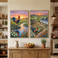 Two colorful countryside rooster paintings hang on a cream wall above a wooden sideboard in a cozy rustic kitchen. One painting shows a rooster standing on a rock beside a winding stream surrounded by wildflowers at sunset while the other shows a rooster along a path through a farmyard with chickens, a small coop, cottages, and grazing horses under a glowing sunset sky.