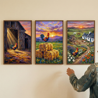Three framed artworks hang on a plain wall, with a person in a denim jacket reaching towards the rightmost one. The left piece features a rooster at a barn entrance with dramatic sunbeams. The middle artwork shows a rooster on hay bales in a field of flowers under a colorful mountain sunset. The right piece depicts a rural landscape with a farmhouse, grazing horses, and a rooster by a flower-lined path. All three scenes share a richly textured, vibrant, and impressionistic style.