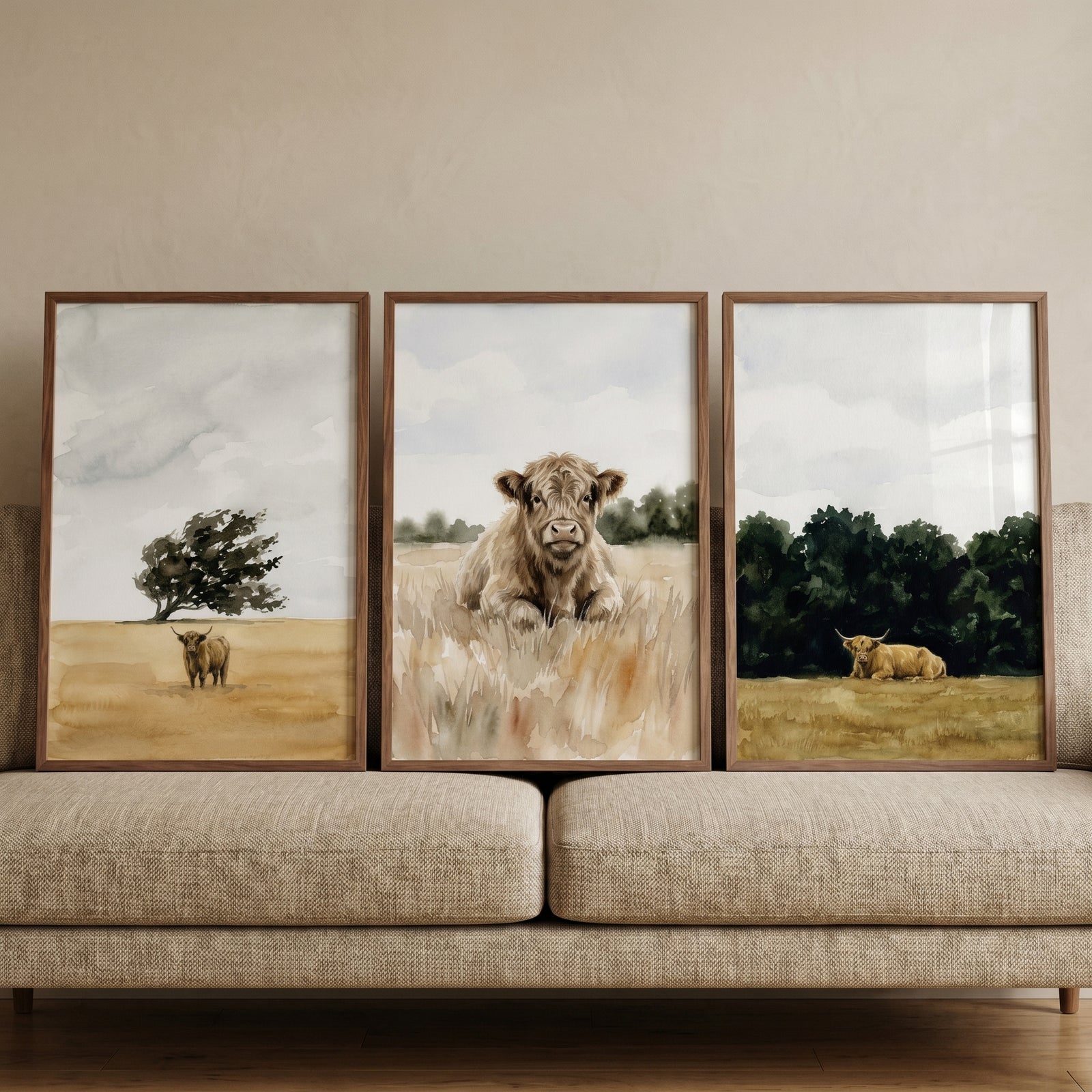 Farmhouse watercolor highland cow wall art set of 3 displayed in wooden frames above a light tan textured sofa.