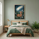 An elegantly styled bedroom features sage green vertical wood-paneled walls and a light wood bed. Above the bed hangs a framed vertical illustration depicting a small, spotted fawn resting in a dark, lush forest filled with ferns and white lilies. In the deep blue night sky above, a bright comet with a gentle, smiling face on its moon-like head streaks across. The bed is dressed in layers of sage green and beige linens with a thick, cream-colored knit throw draped over the end. To the left, a matching woode
