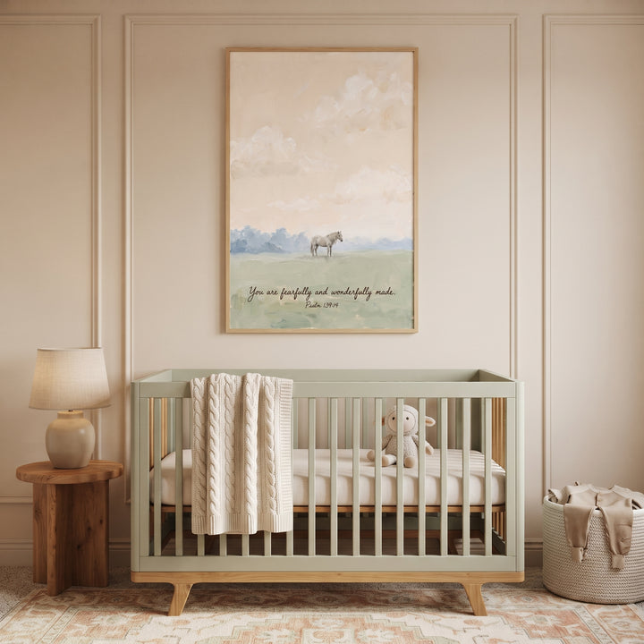 Sage crib in a nursery below fearfully wonderfully made horse wall art featuring a soft landscape and scripture.