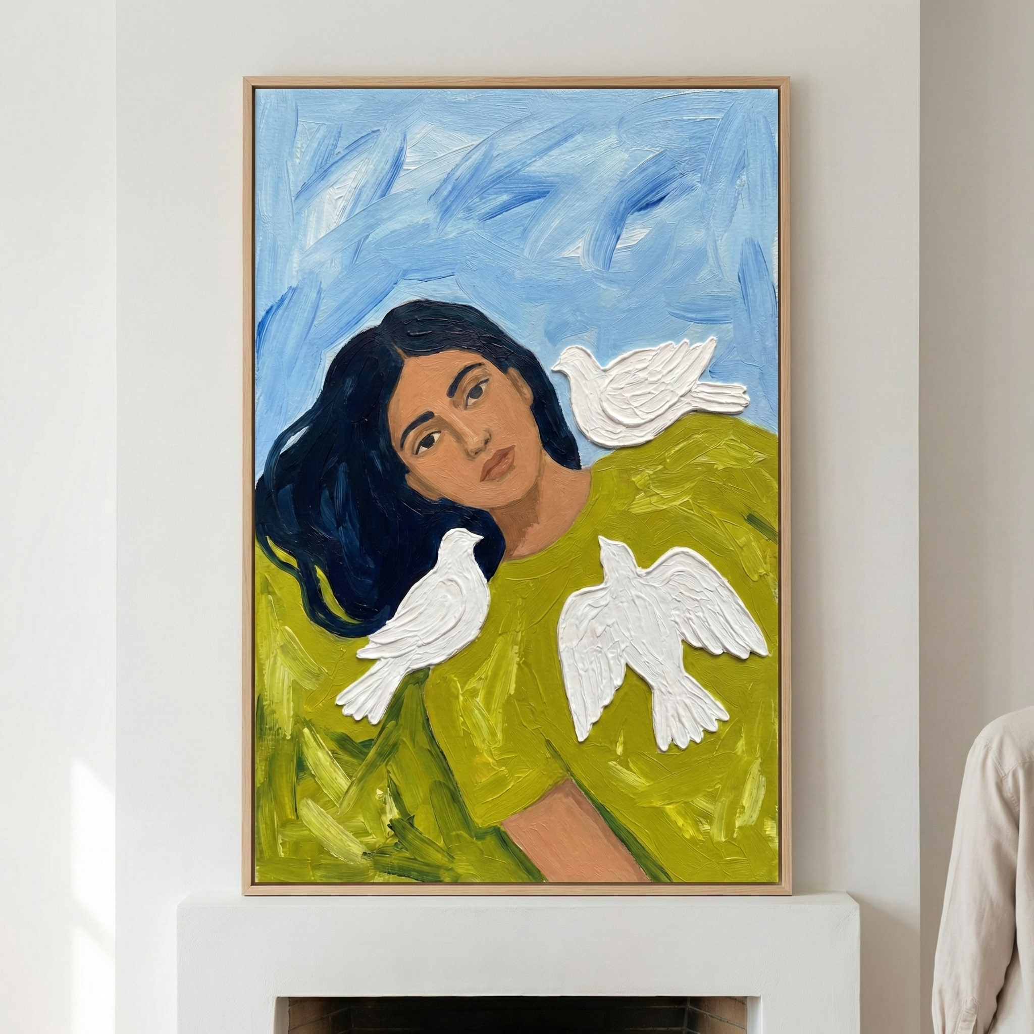 A vertically oriented artwork featuring a person with dark hair and a thoughtful expression. They are wearing a bright, lime-green top. Three white birds, rendered with thick, raised texture, are positioned around the figure: one on the shoulder, one over the chest, and one above the head. The background consists of light blue and white expressive strokes. The piece is framed in natural light wood and hangs on a plain white wall above a minimalist mantelpiece.