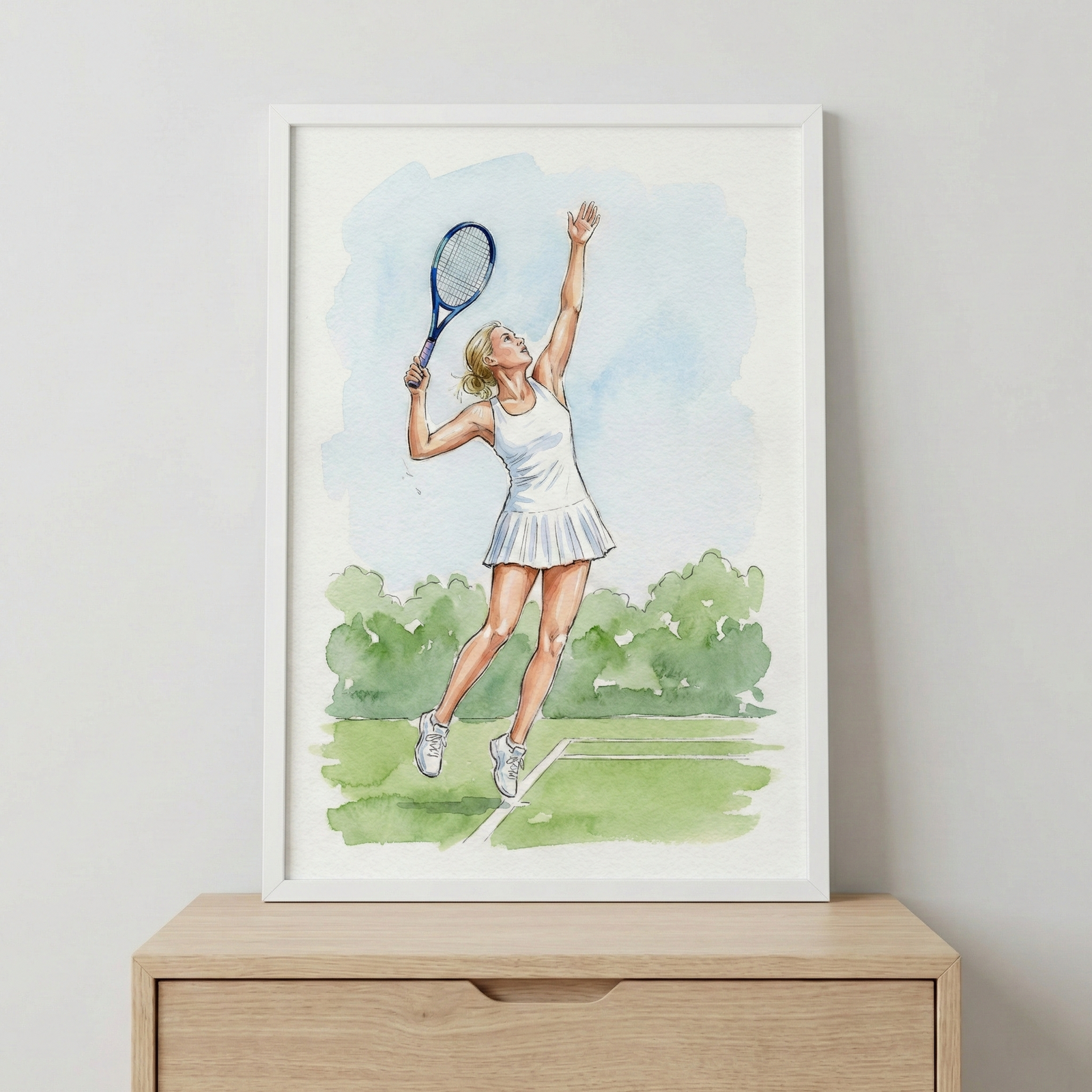 A framed watercolor illustration of a female tennis player in a white athletic dress. She is captured in a dynamic pose on a green court, holding a tennis racket high in the air as if preparing for a serve. Behind her, soft green foliage and a pale blue sky complete the scene. The artwork is housed in a simple white frame, which rests on a light-colored wooden cabinet against a plain gray wall.