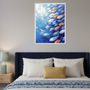 Modern bedroom with a dark blue upholstered bed and a wooden nightstand with a green lamp. Above the bed hangs a framed painting depicting many white, orange, and yellow fish swimming in dynamic blue water.