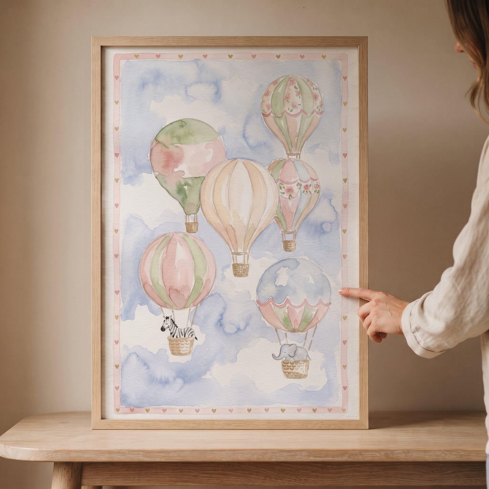 Watercolor floral hot air balloon wall art featuring a zebra and elephant in a wood frame, resting on a table.
