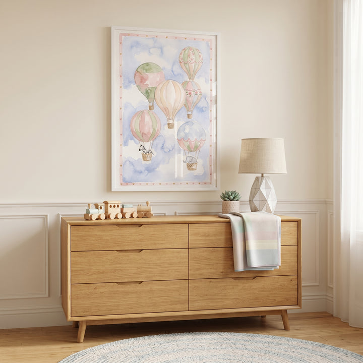 Floral hot air balloon wall art hangs above a wooden dresser with a lamp and toy train in a cozy, neutral nursery.