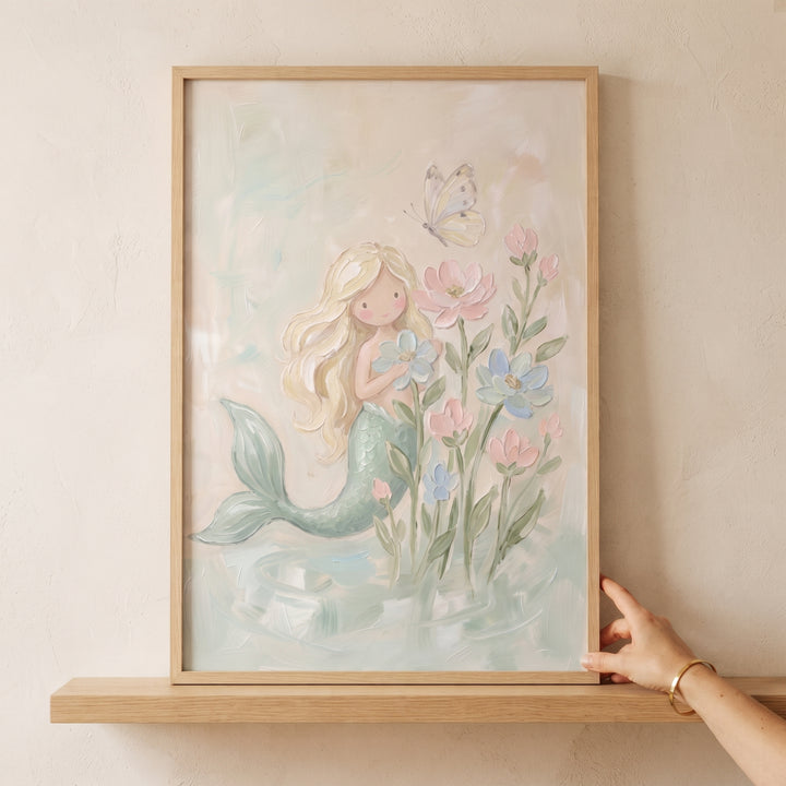 Floral pastel blonde mermaid wall art in a wooden frame shows a mermaid with a green tail, pink flowers, and a butterfly.