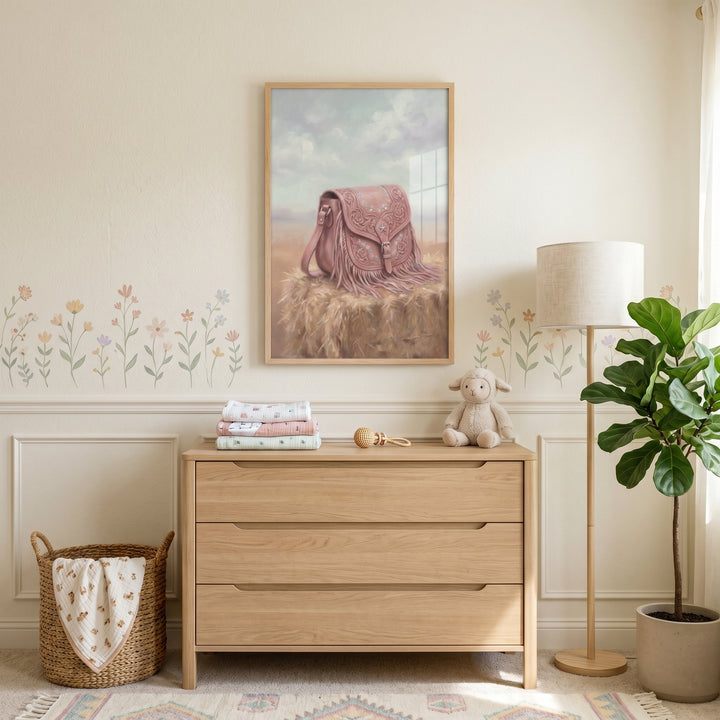 Floral pink fringe bag wall art hangs in a nursery above a wooden dresser with a plush lamb, lamp, and potted plant.