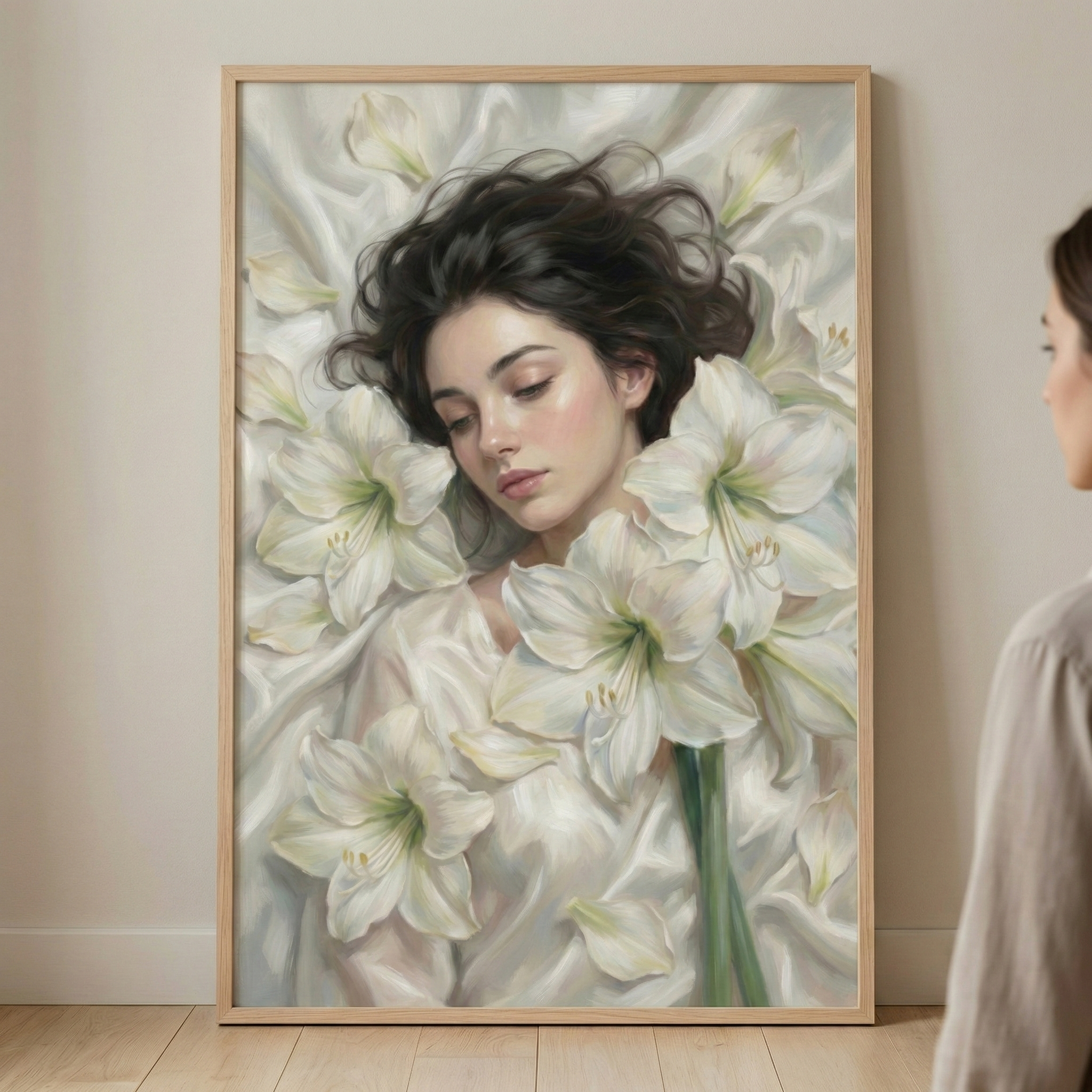 A large, framed vertical artwork leans against a light-colored wall on a wooden floor. The image portrays a young woman with dark, flowing hair resting among several large, blooming white lilies. She has a serene expression and closed eyes, with soft light illuminating her delicate features. The woman is draped in flowing white fabric that blends seamlessly with the white flower petals. In the foreground on the right, the shoulder of a person is partially visible as they view the piece.