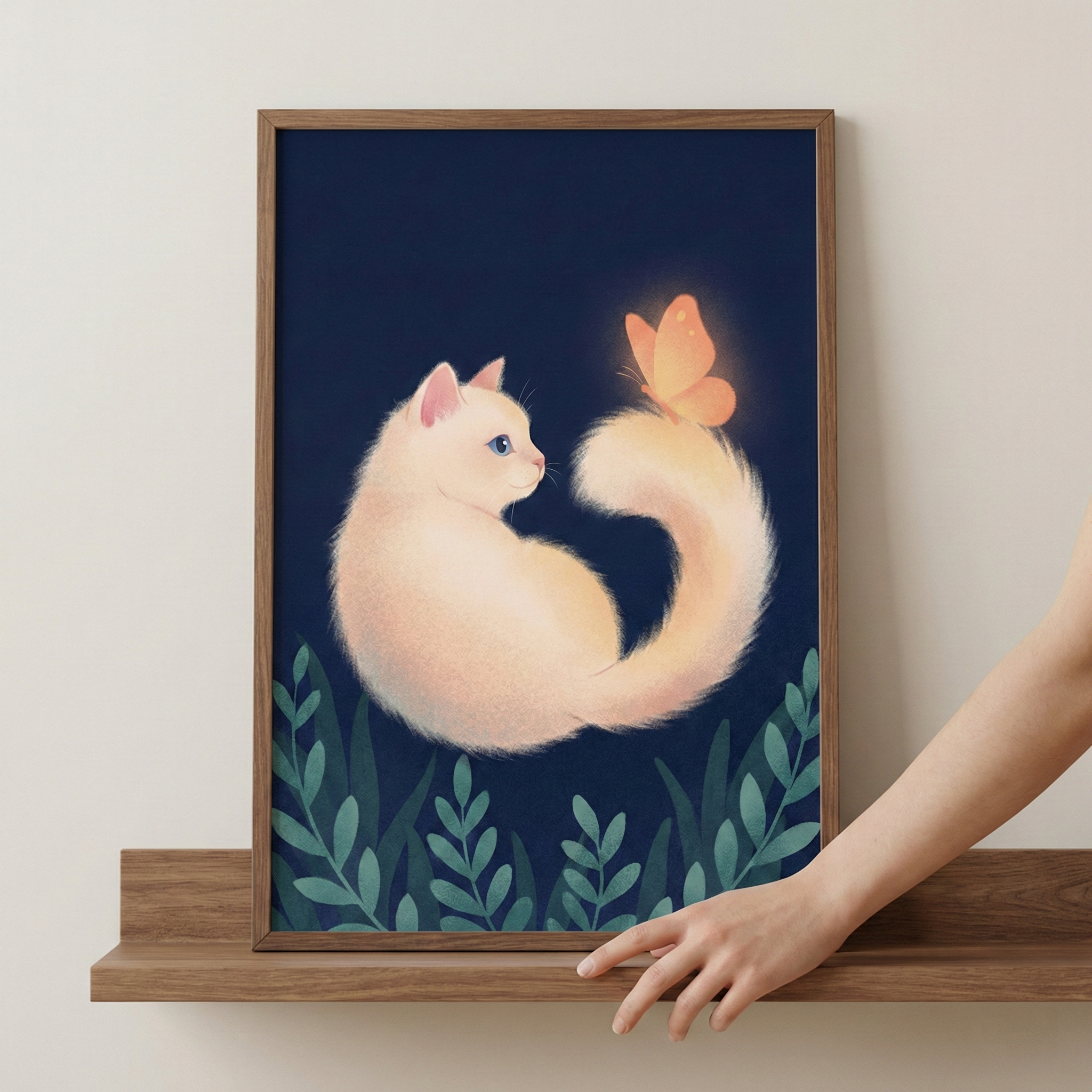 A framed illustration shows a fluffy, cream-colored cat with bright blue eyes sitting against a dark navy blue background. The cat's long tail curves upward, and a glowing orange butterfly rests on its tip. Stylized green leaves line the bottom of the scene. The wooden frame sits on a matching wooden shelf against a plain wall. A person's hand reaches in from the right, touching the bottom edge of the frame.